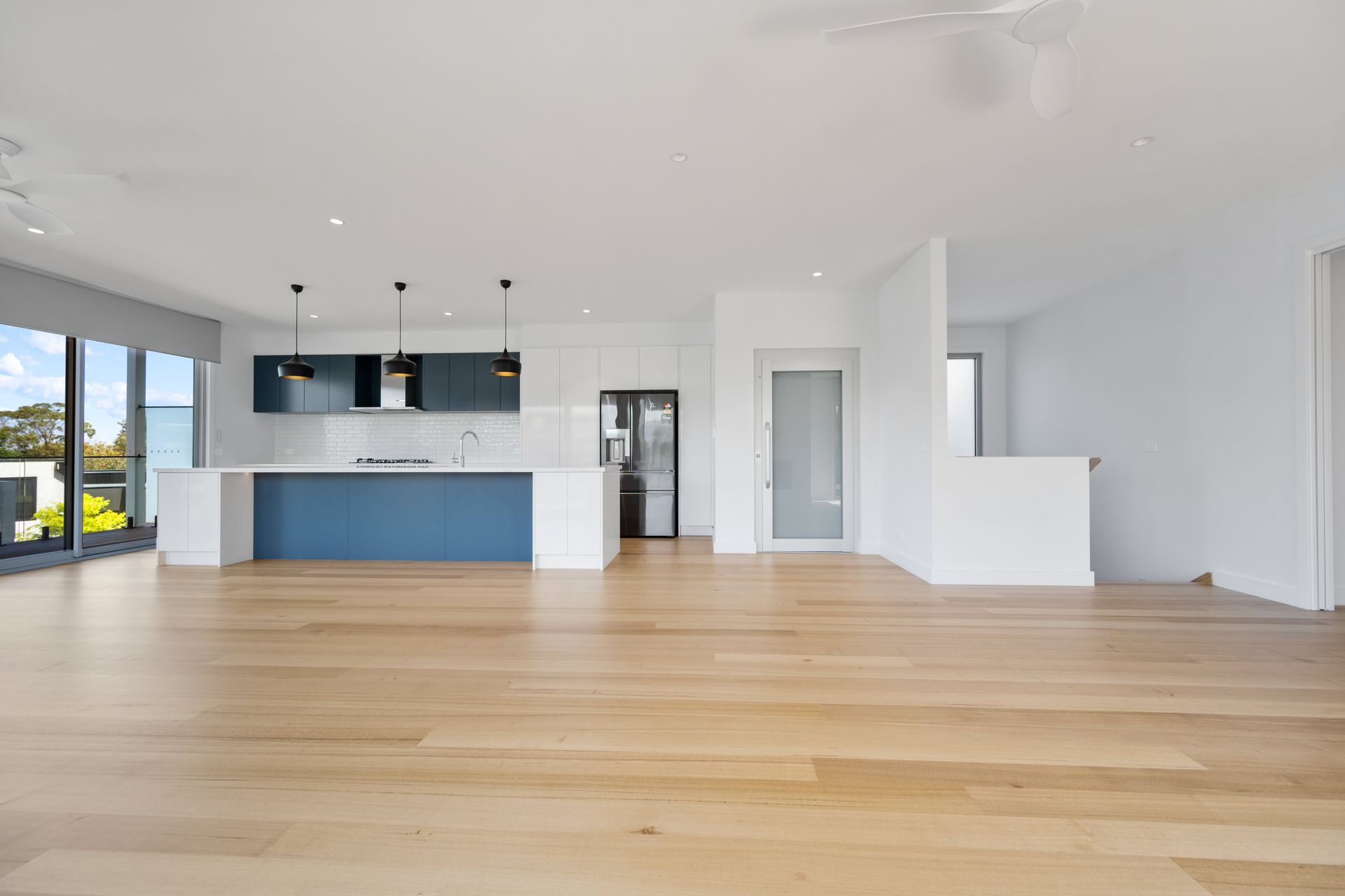 Open-concept kitchen and living space with blue cabinets, a white island, and light wooden floors. Large windows on the left.
