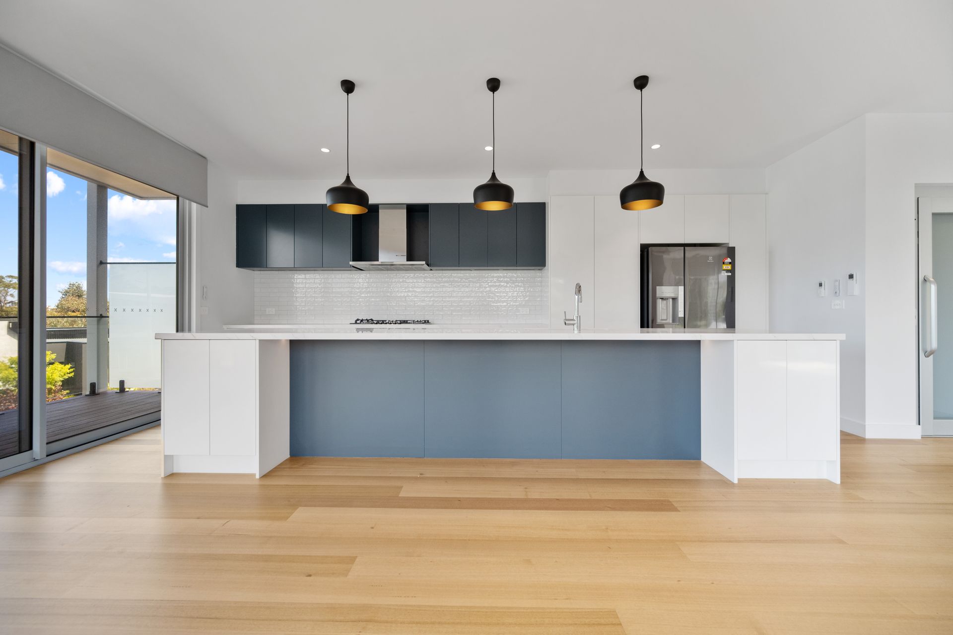 Modern kitchen with a blue island and cabinetry, three pendant lights, and light wood flooring.
