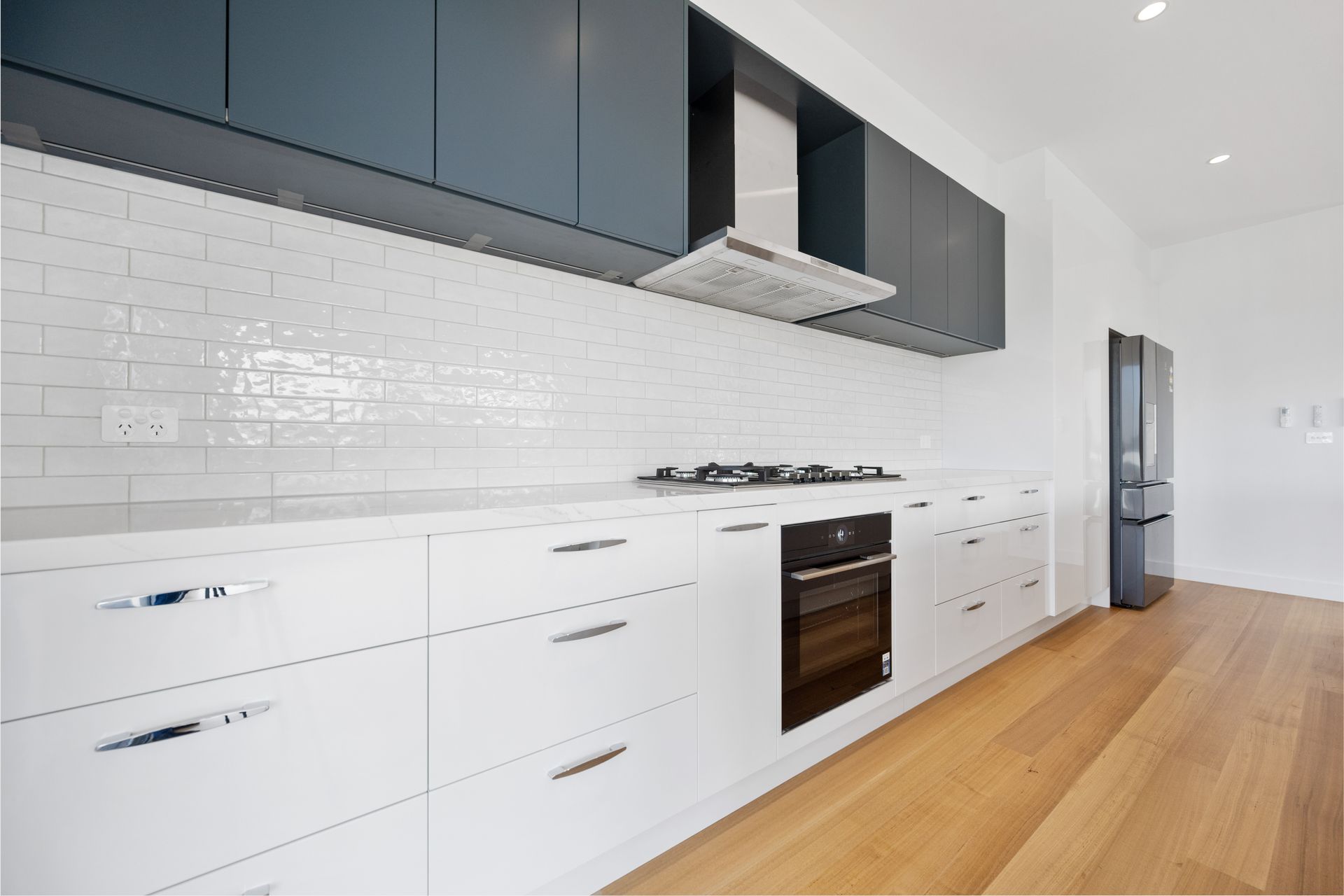 Modern kitchen with white cabinets, white subway tile backsplash, dark blue upper cabinets, and stainless steel appliances.