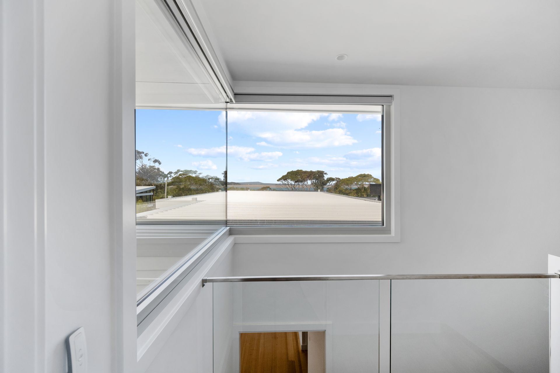 A bright interior room with a large window offering a view of a beach under a blue sky. Glass railings and a door are also visible.