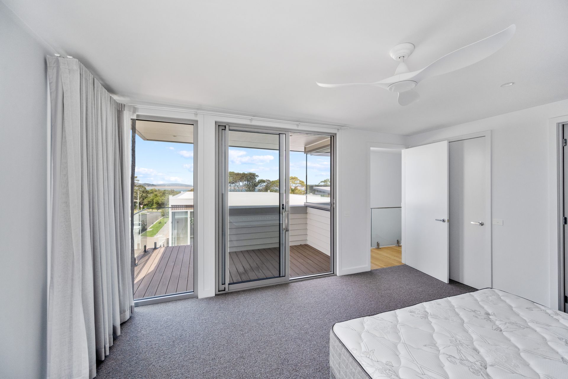 A bedroom with sliding glass doors leading to a deck. White walls, gray carpet, and a bed.