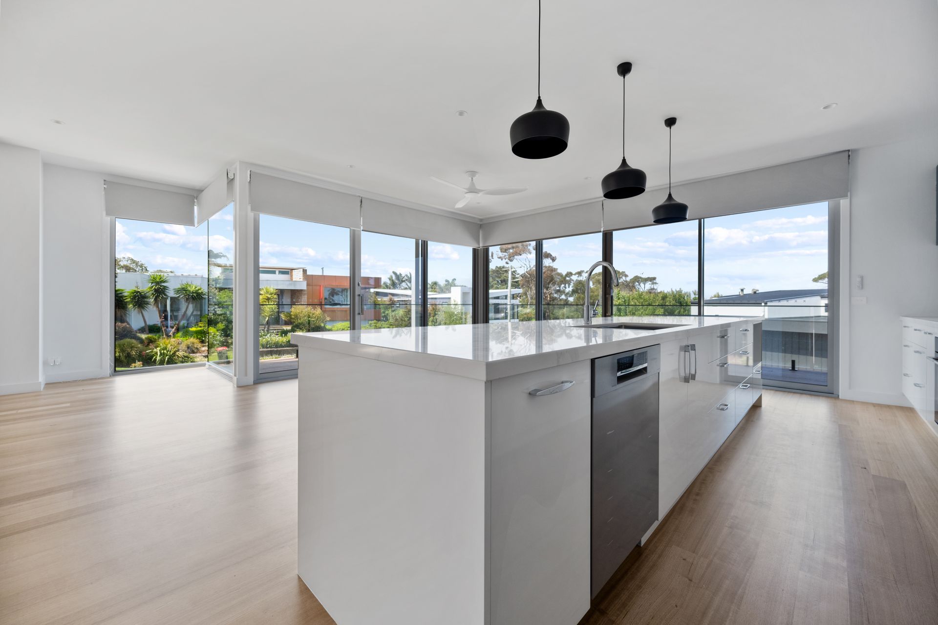 Spacious modern kitchen with white island, built-in dishwasher, and floor-to-ceiling windows overlooking a lush outdoor area.