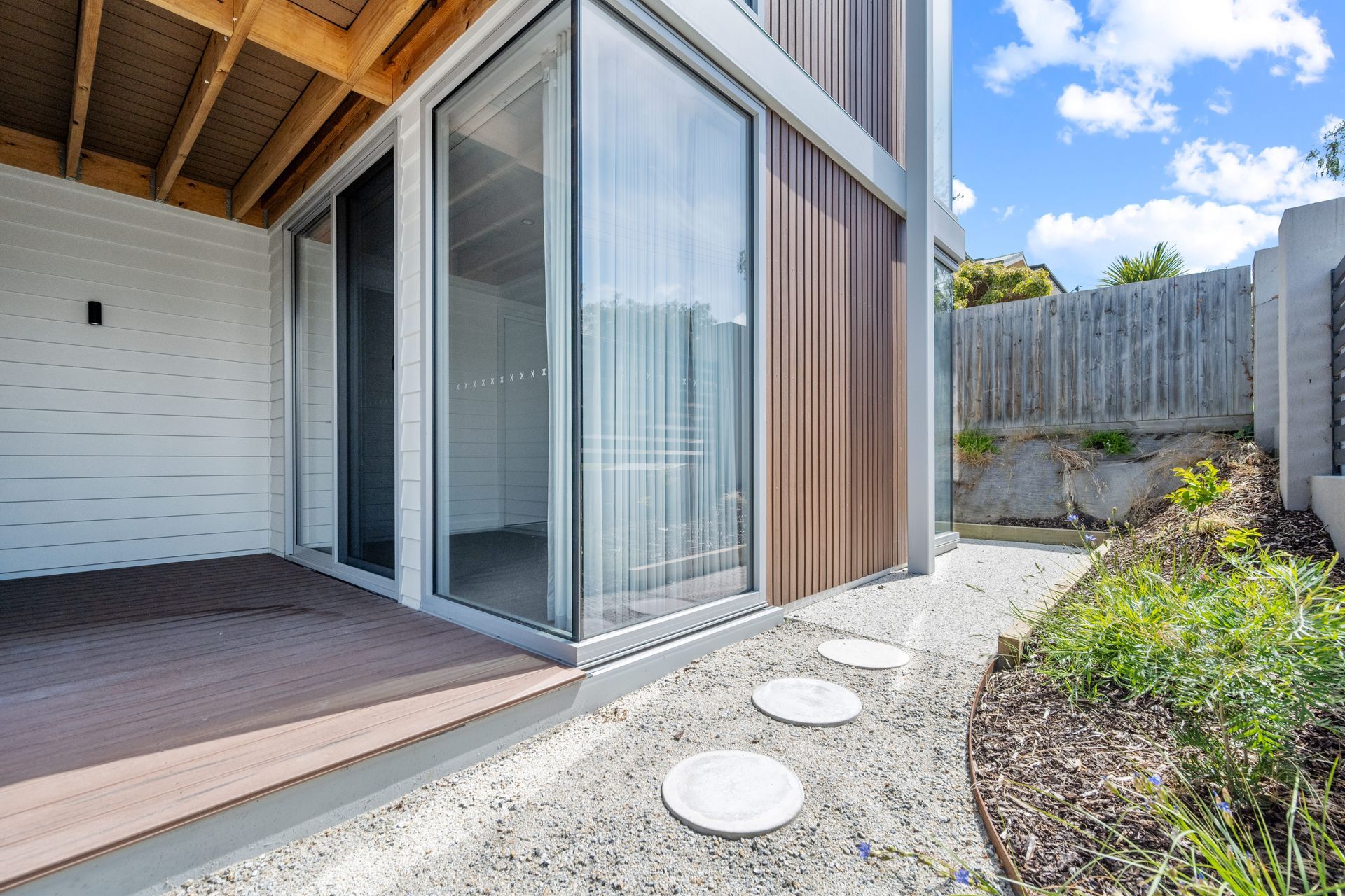 Exterior view of a modern building with glass doors, wooden siding, and a small pathway leading to a fence.