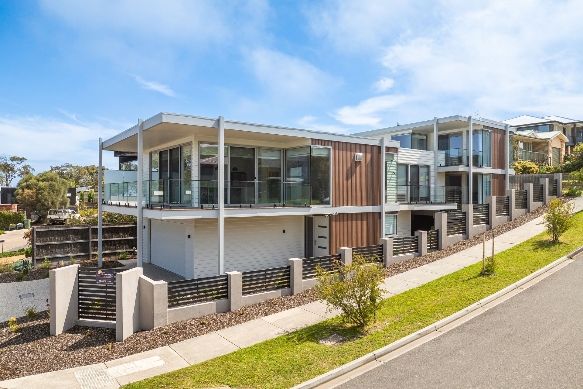 Modern multi-story house with glass balconies and a sloped lawn, on a sunny day.