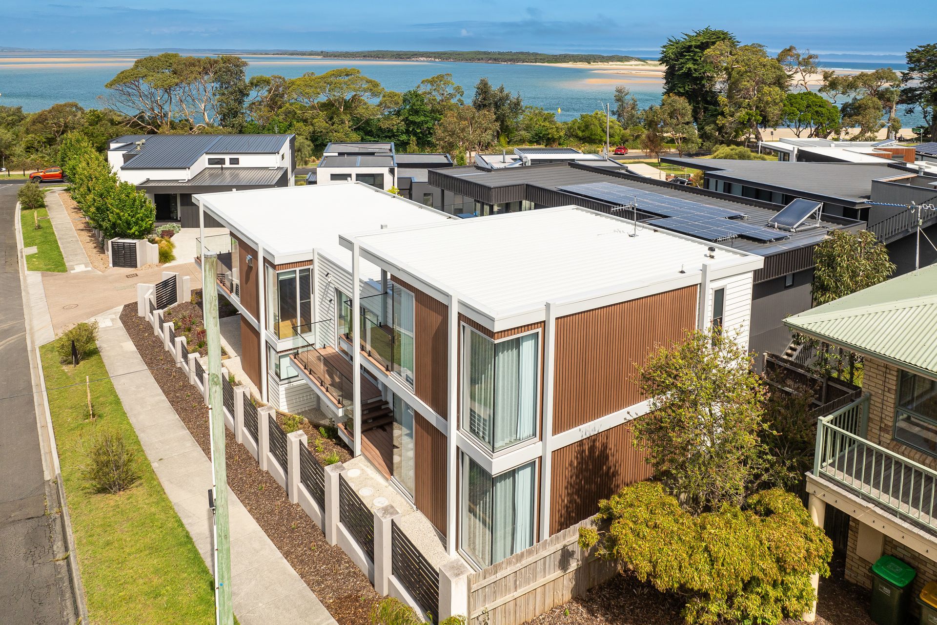 Modern two-story homes with brown siding and large windows, near a waterway and a coastal town.