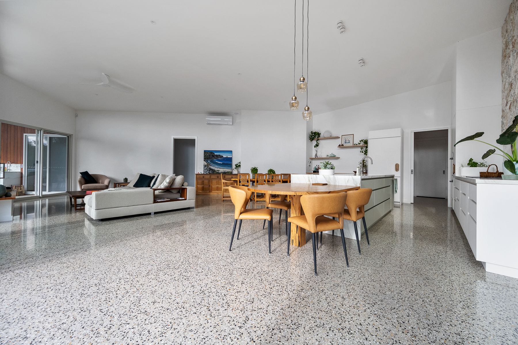 Open-plan living space with terrazzo flooring, a dining area with wooden chairs, and a white kitchen island.