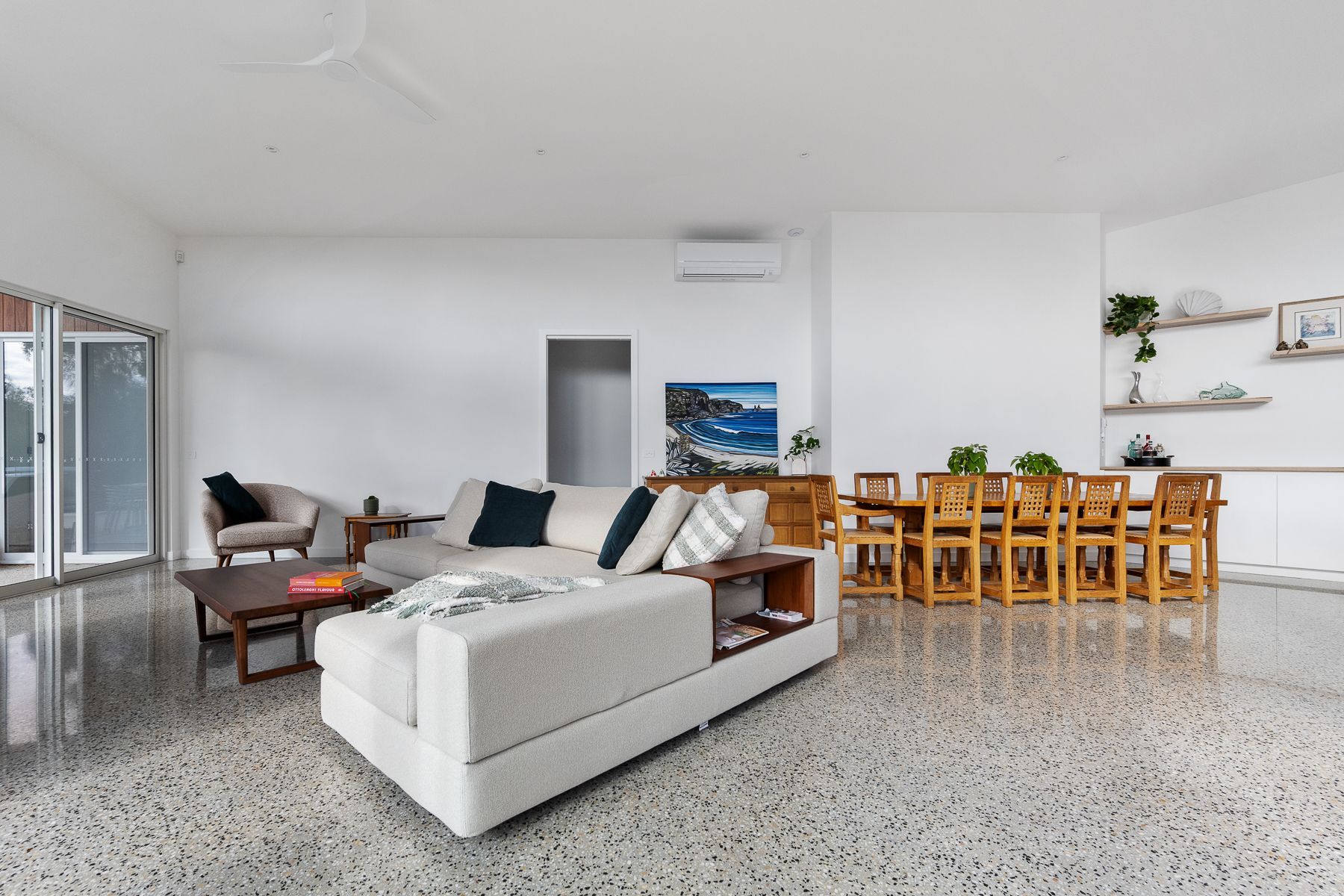 Spacious, modern living and dining area with a light grey sectional sofa, a wooden dining table, and polished concrete floors.