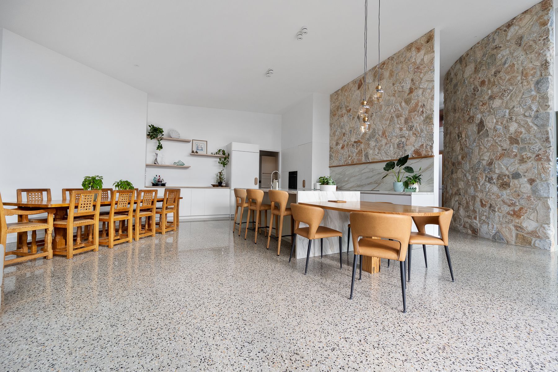 Spacious dining area with long wooden tables, tan chairs, and stone walls, bathed in natural light.