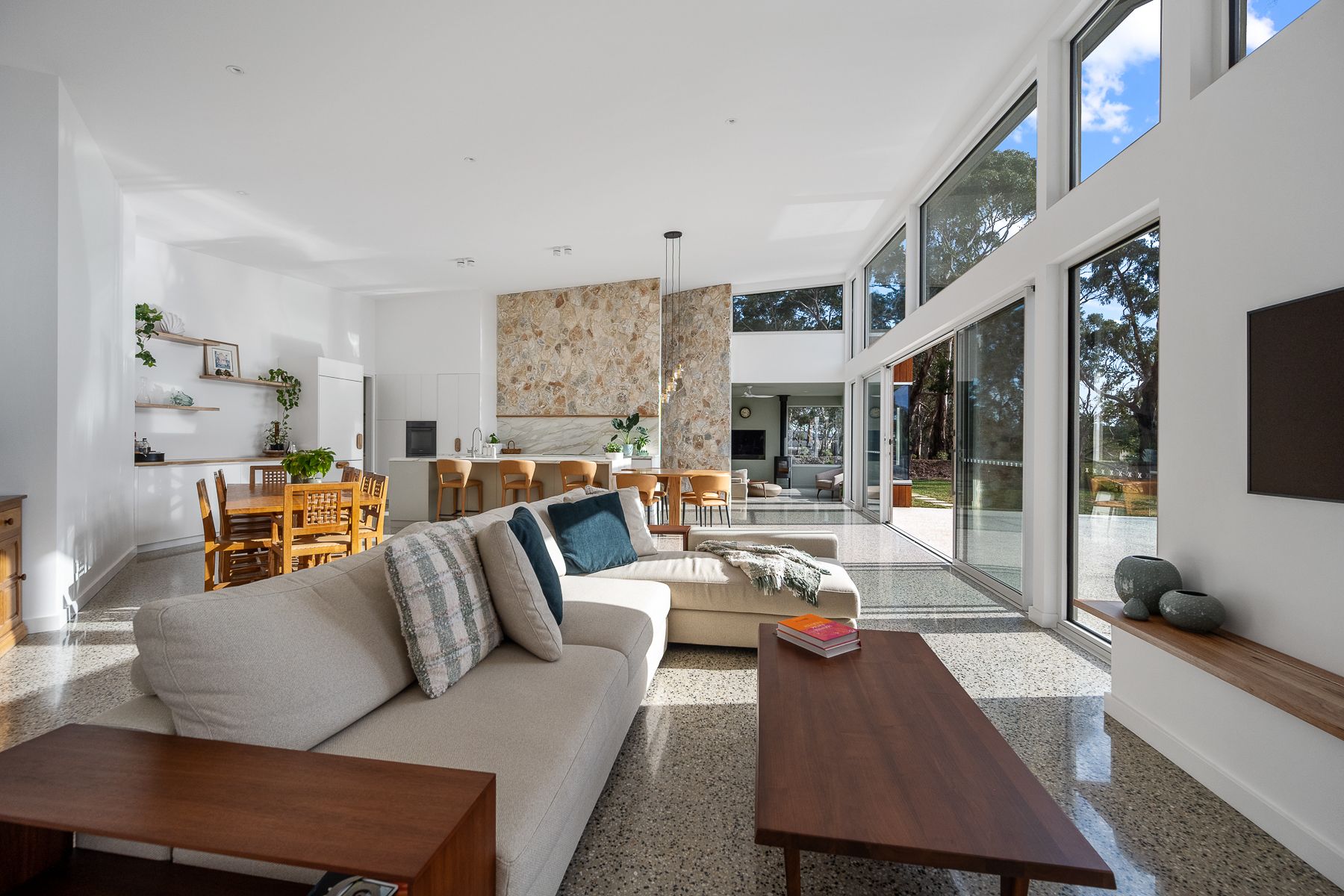 Spacious modern living room with light-colored sofa, stone accent wall, and large windows overlooking the outdoors.
