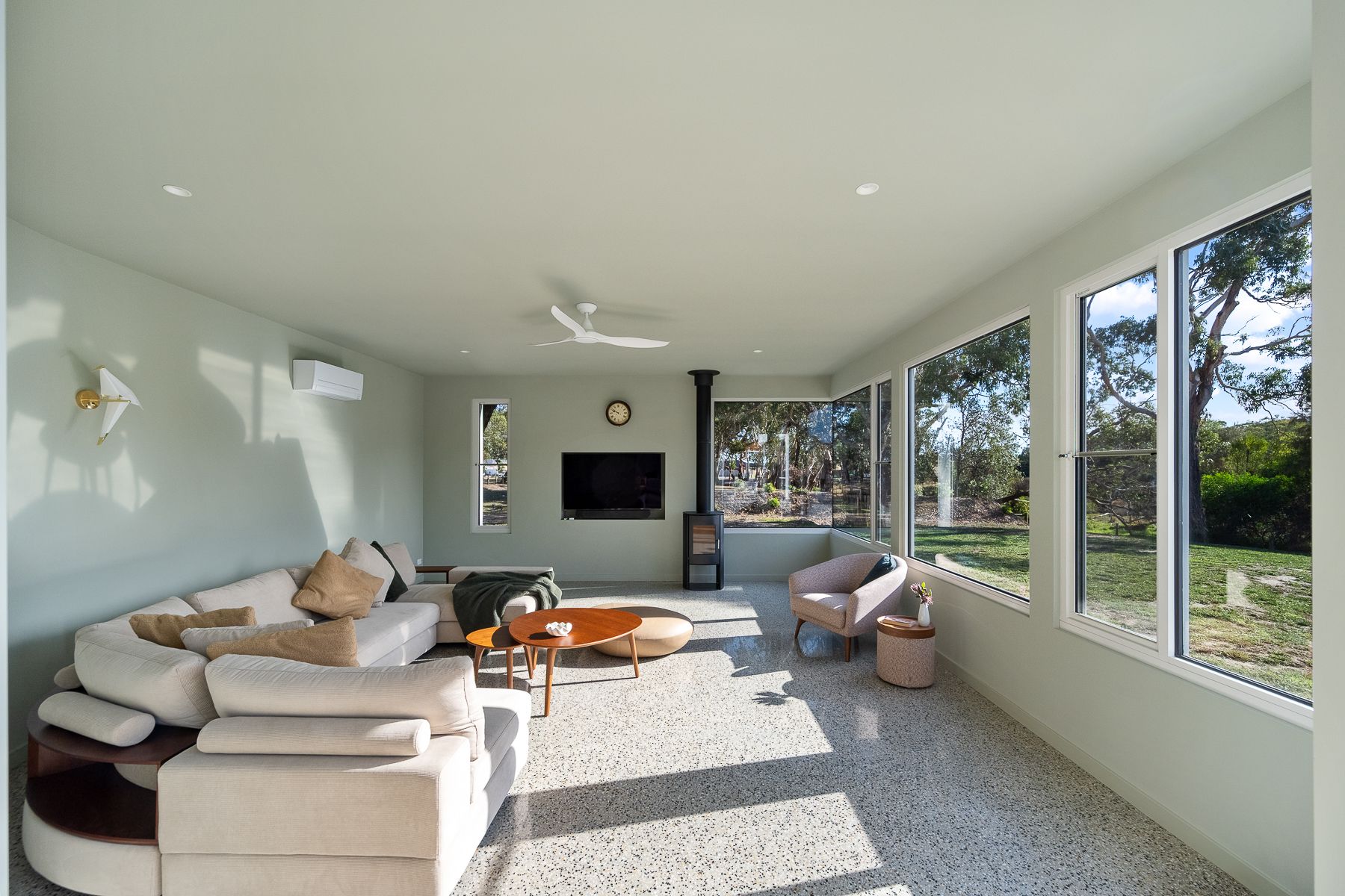 A bright, modern living room with a sectional sofa, fireplace, and large windows overlooking a sunny yard.