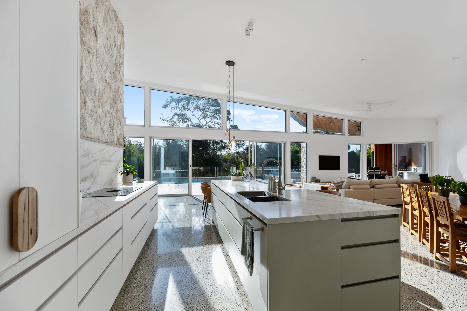 Spacious, modern kitchen with a large island, floor-to-ceiling windows, and a view of the outdoors. Bright, with white cabinets and speckled flooring.