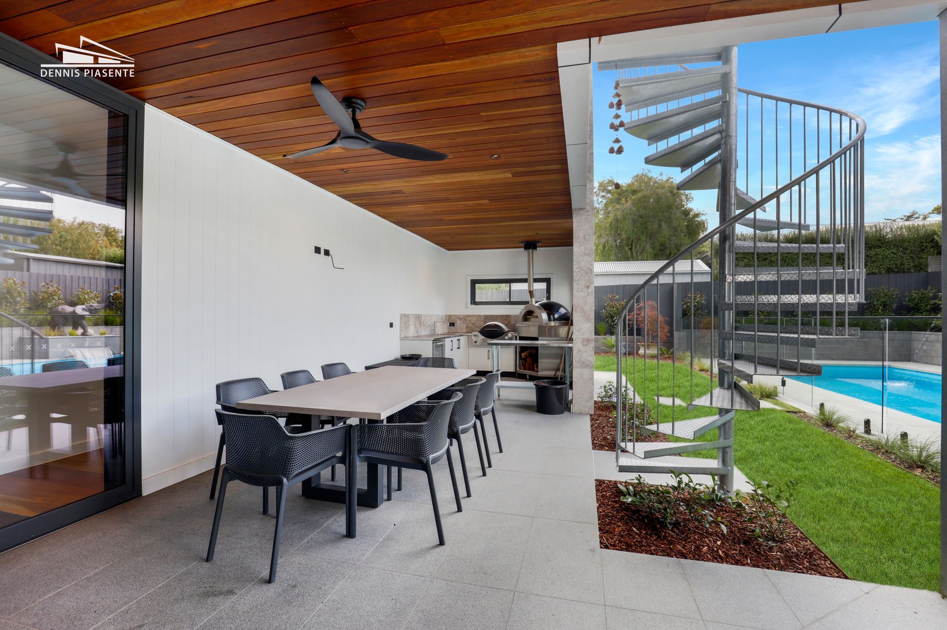 A patio with a table and chairs and a spiral staircase leading to a pool.