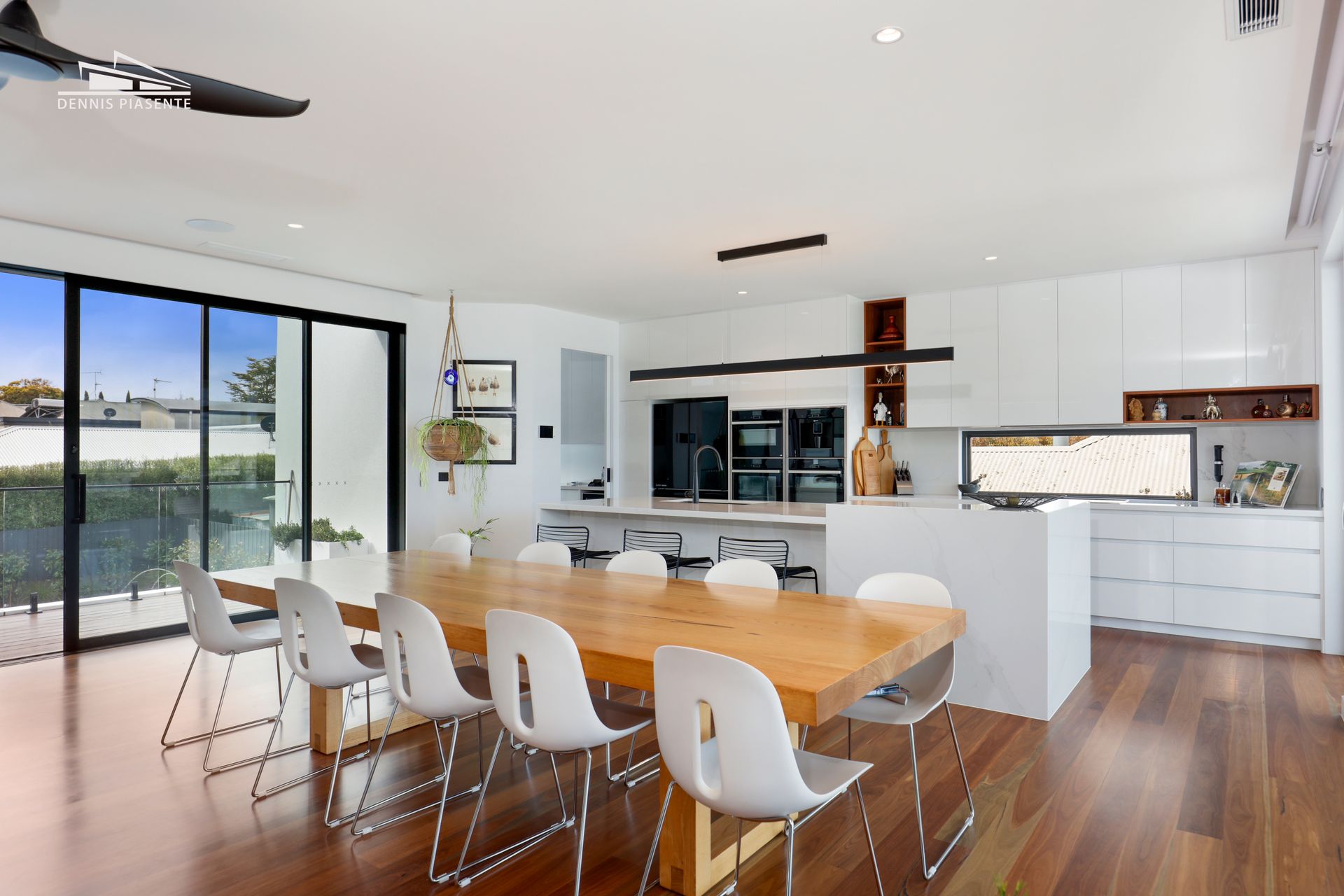 A dining room with a long wooden table and white chairs.