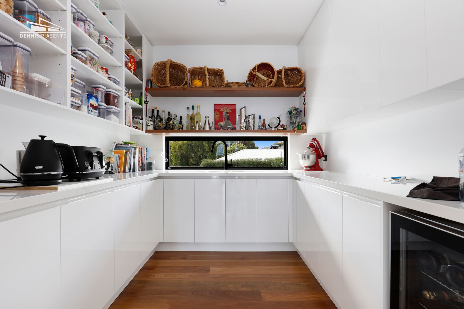 A kitchen with white cabinets , wooden floors , a refrigerator and a window.