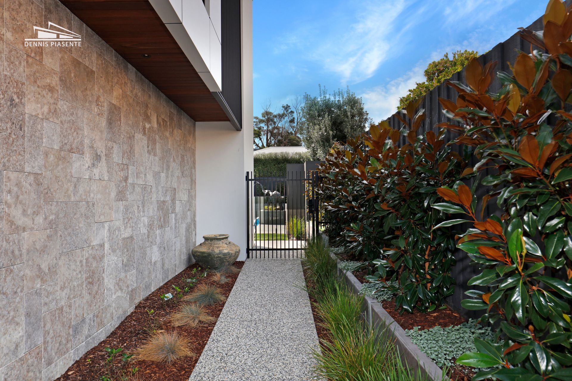 A walkway leading to a house with a fence and bushes.
