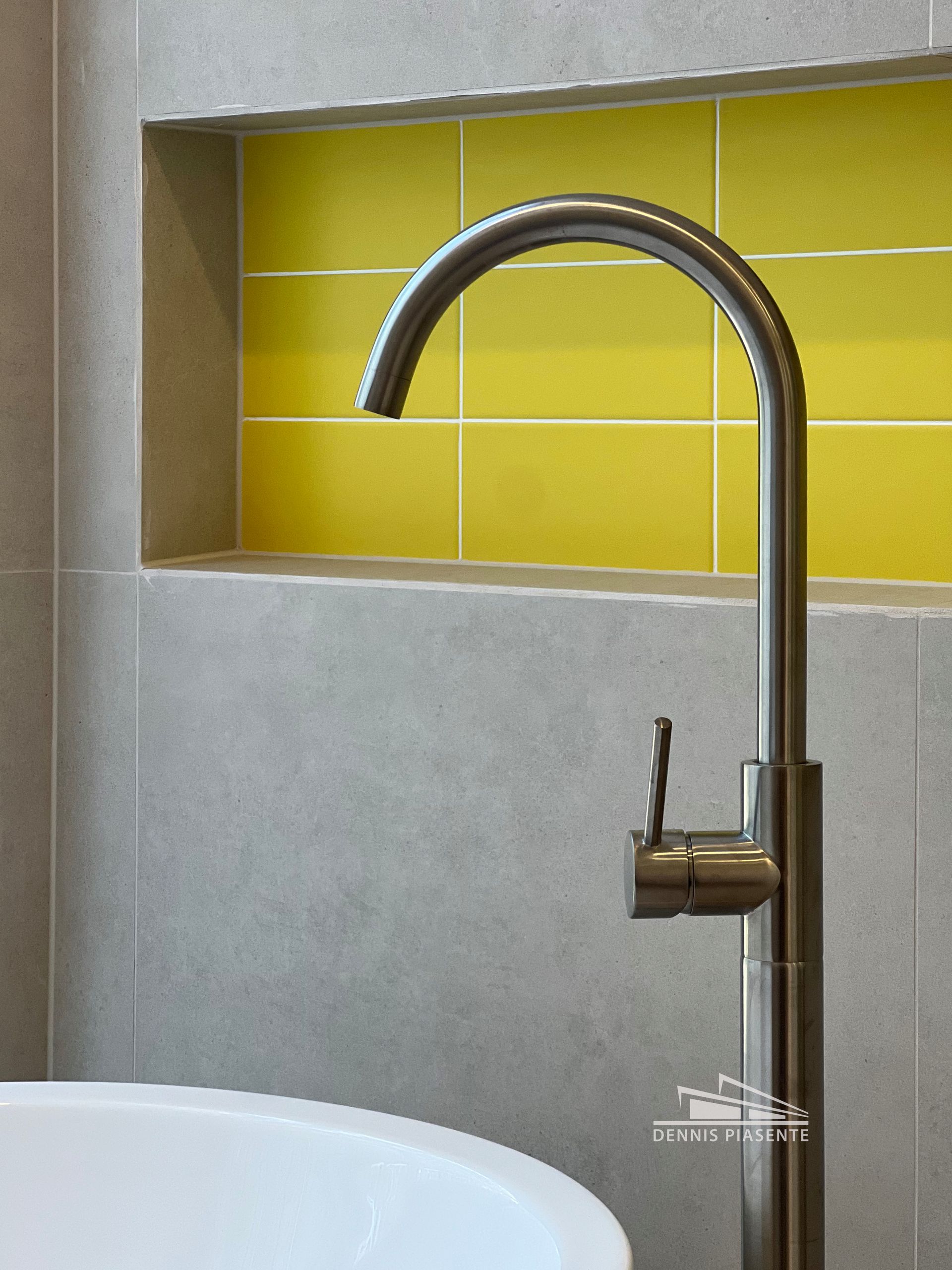 A bathroom with yellow tiles and a stainless steel faucet