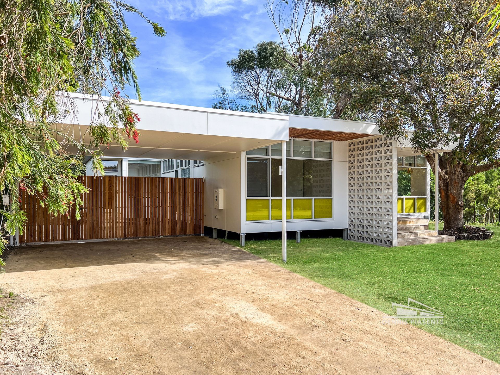A white house with a wooden fence and a driveway in front of it.
