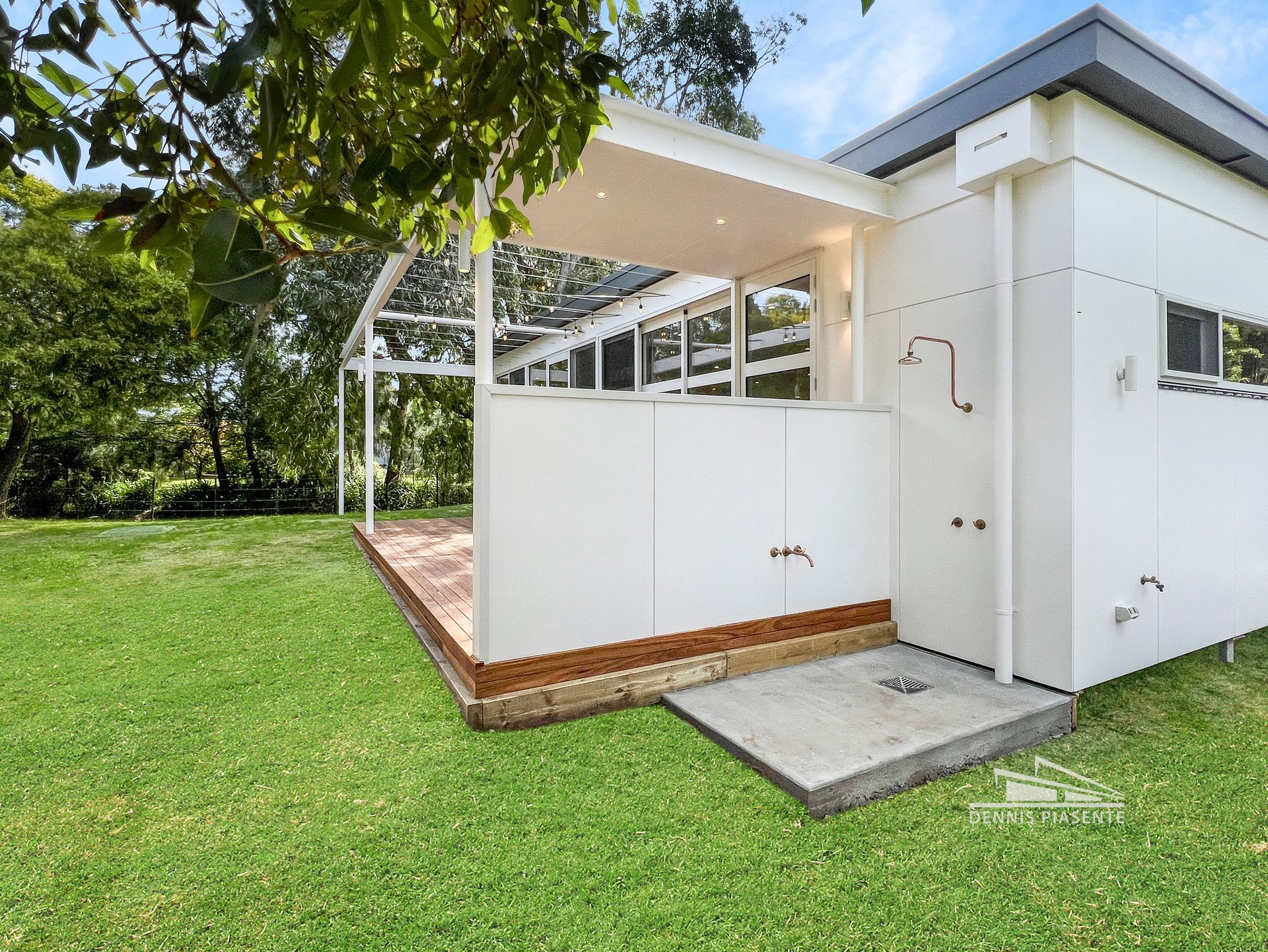 A white building with a shower on the side of it is sitting on top of a lush green field.