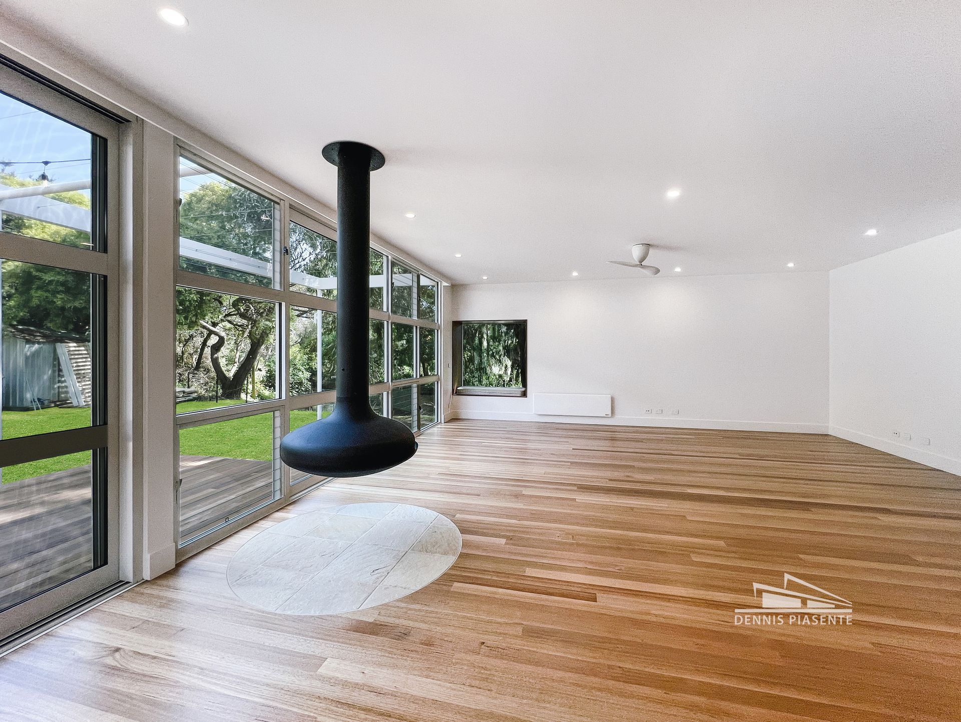 An empty living room with hardwood floors and a fireplace hanging from the ceiling.