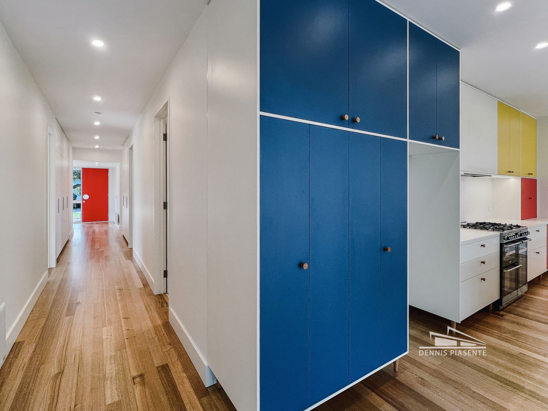 A hallway leading to a kitchen with blue cabinets and a red door.