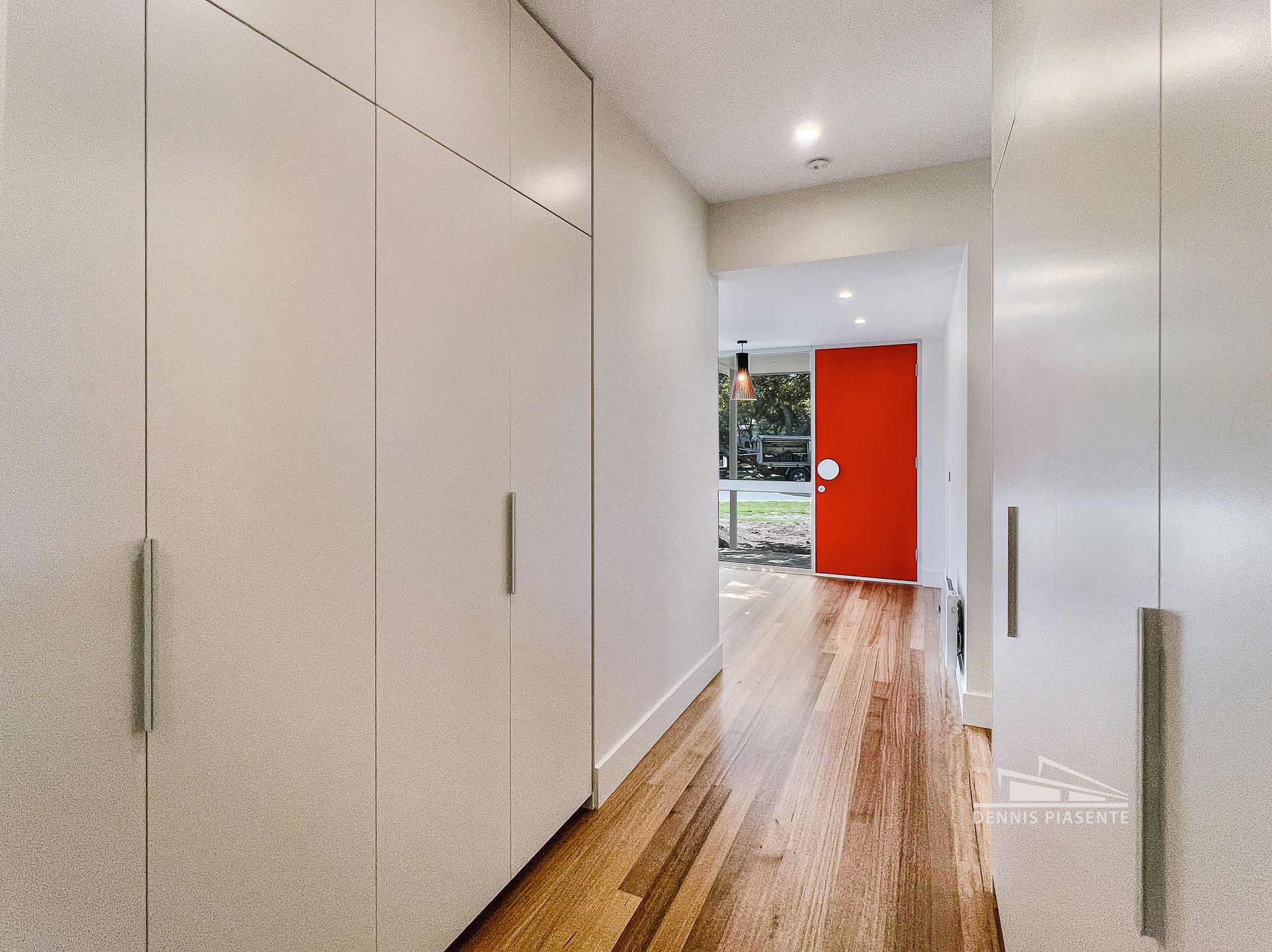 A hallway with white cabinets and a red door