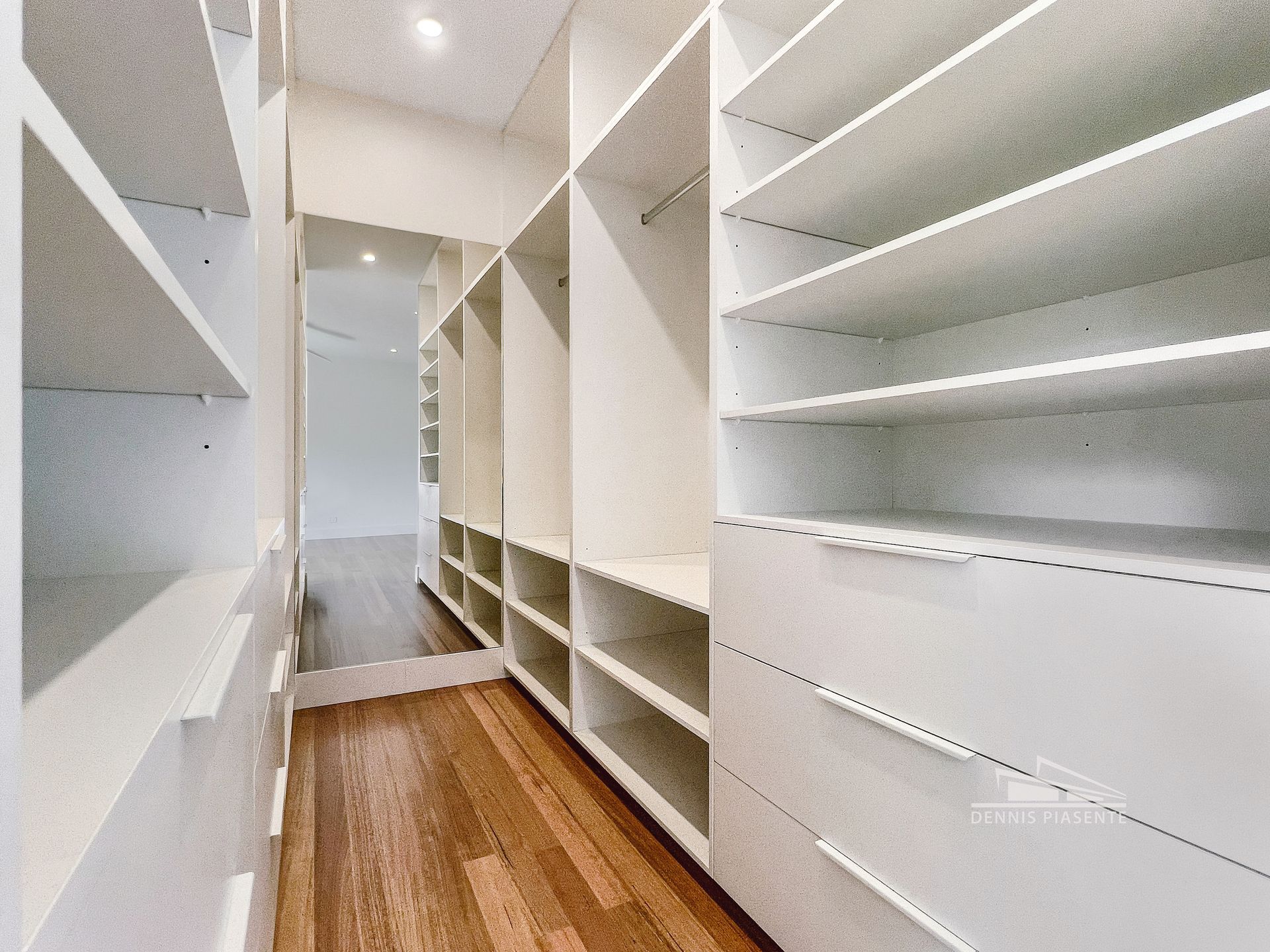 A walk in closet with lots of shelves and drawers and a mirror.