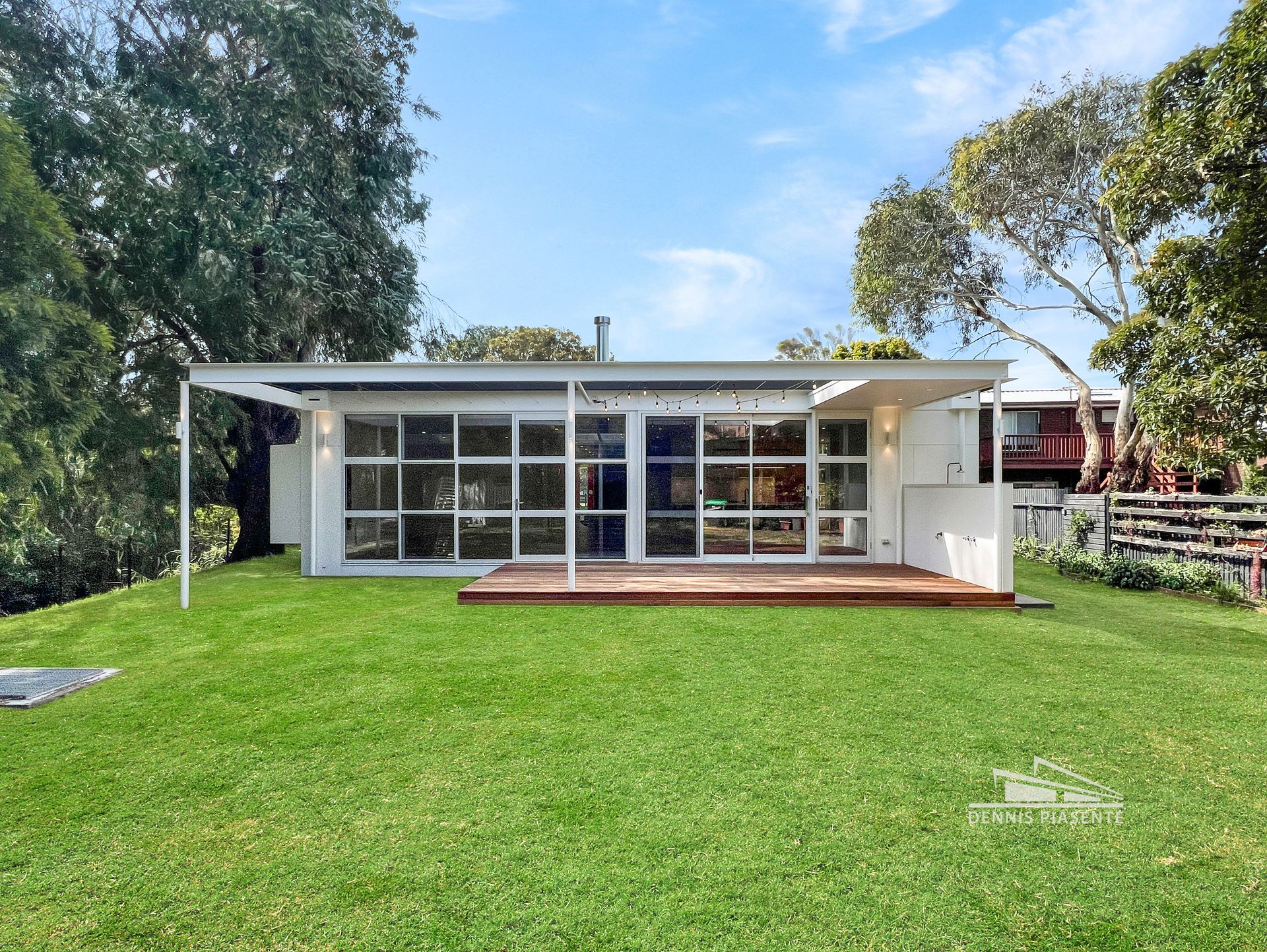 A small white house with a lot of windows is sitting on top of a lush green lawn.