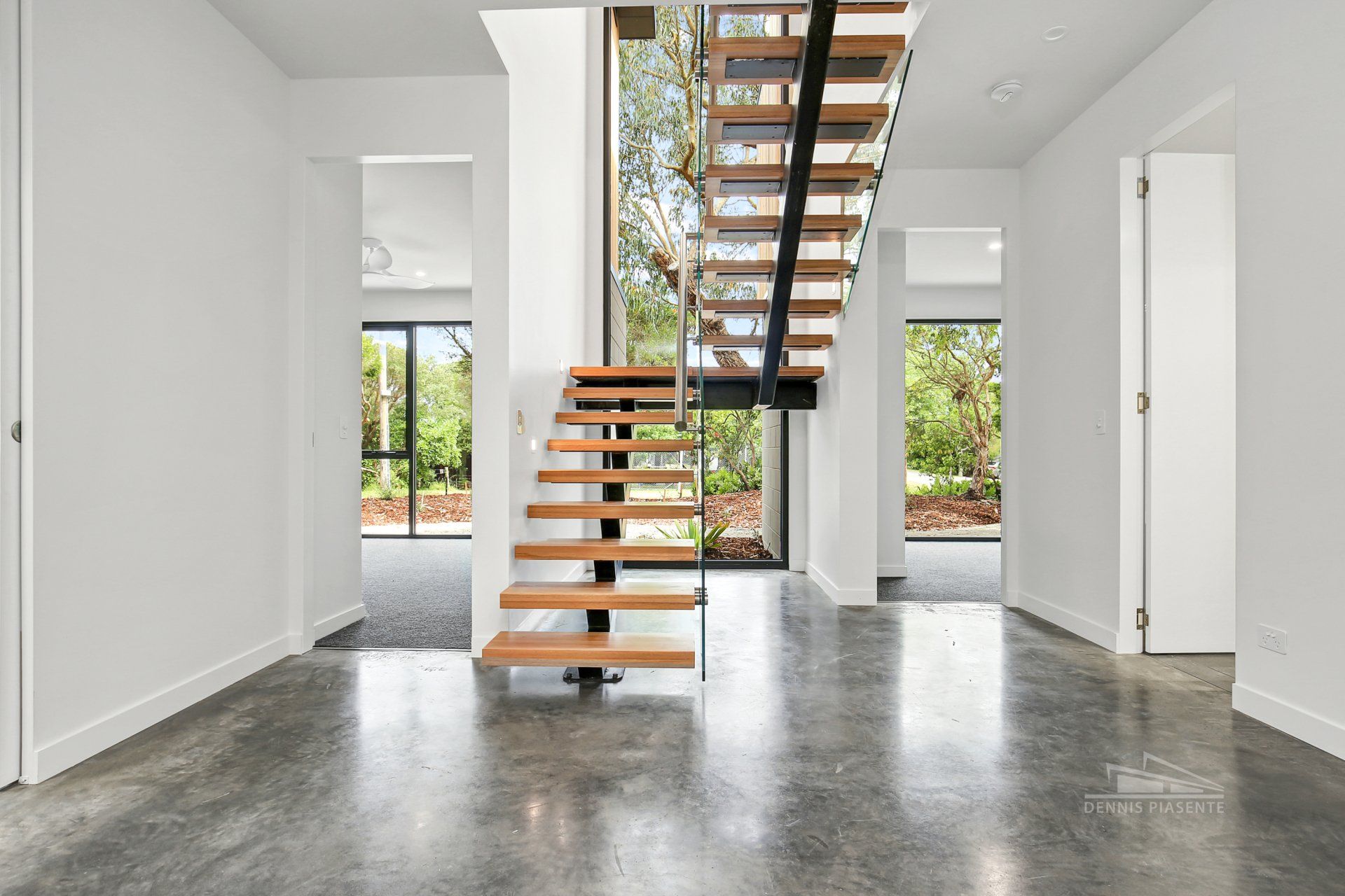 An empty hallway with a wooden staircase and a concrete floor.
