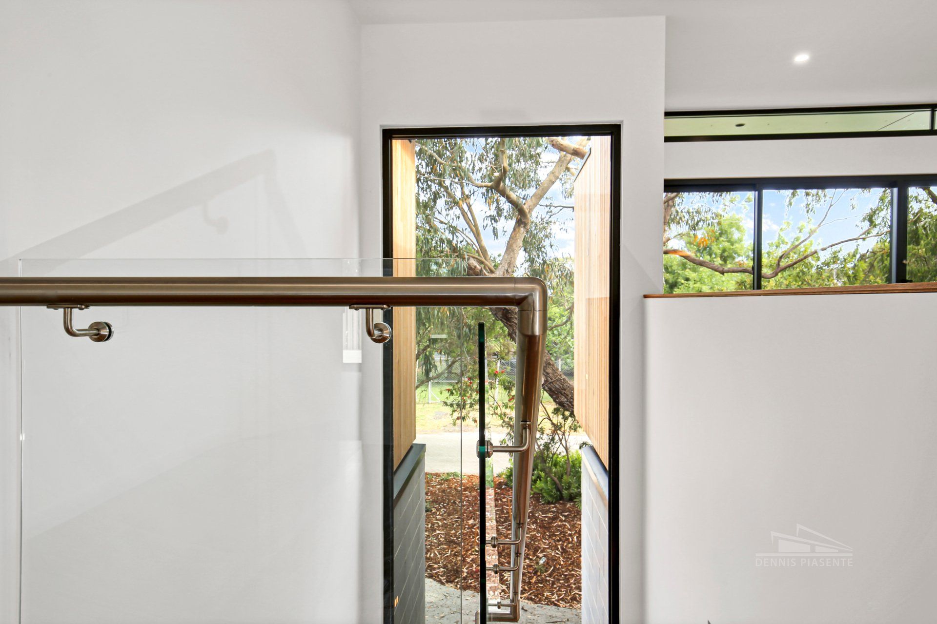 A staircase with a glass railing and a window with a view of a tree.