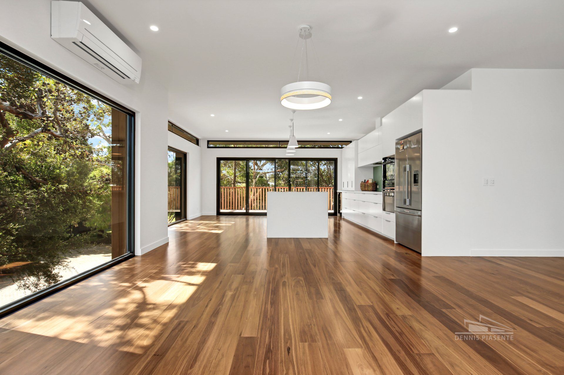 A large empty room with hardwood floors and a kitchen.