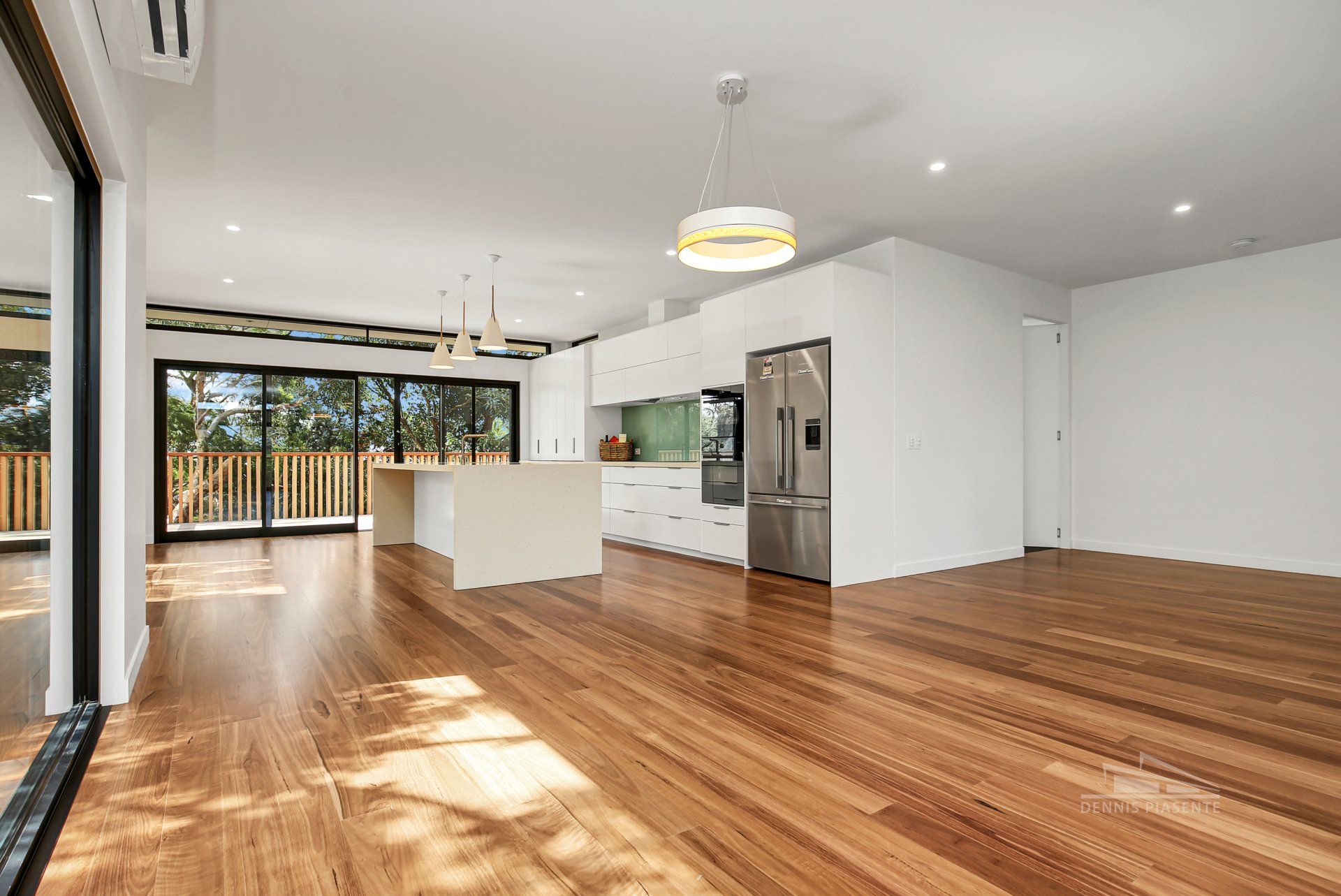 A large empty room with hardwood floors and a kitchen.