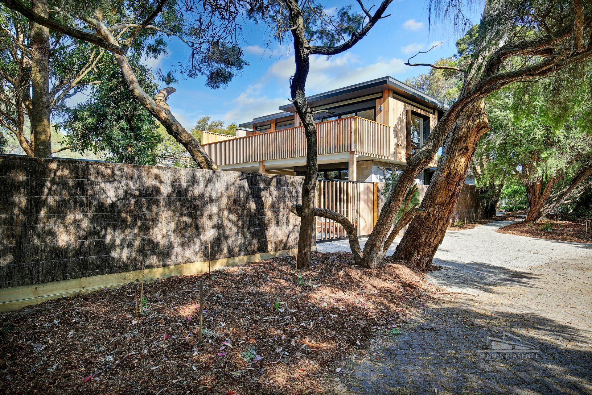 A house with a deck is surrounded by trees and a fence.
