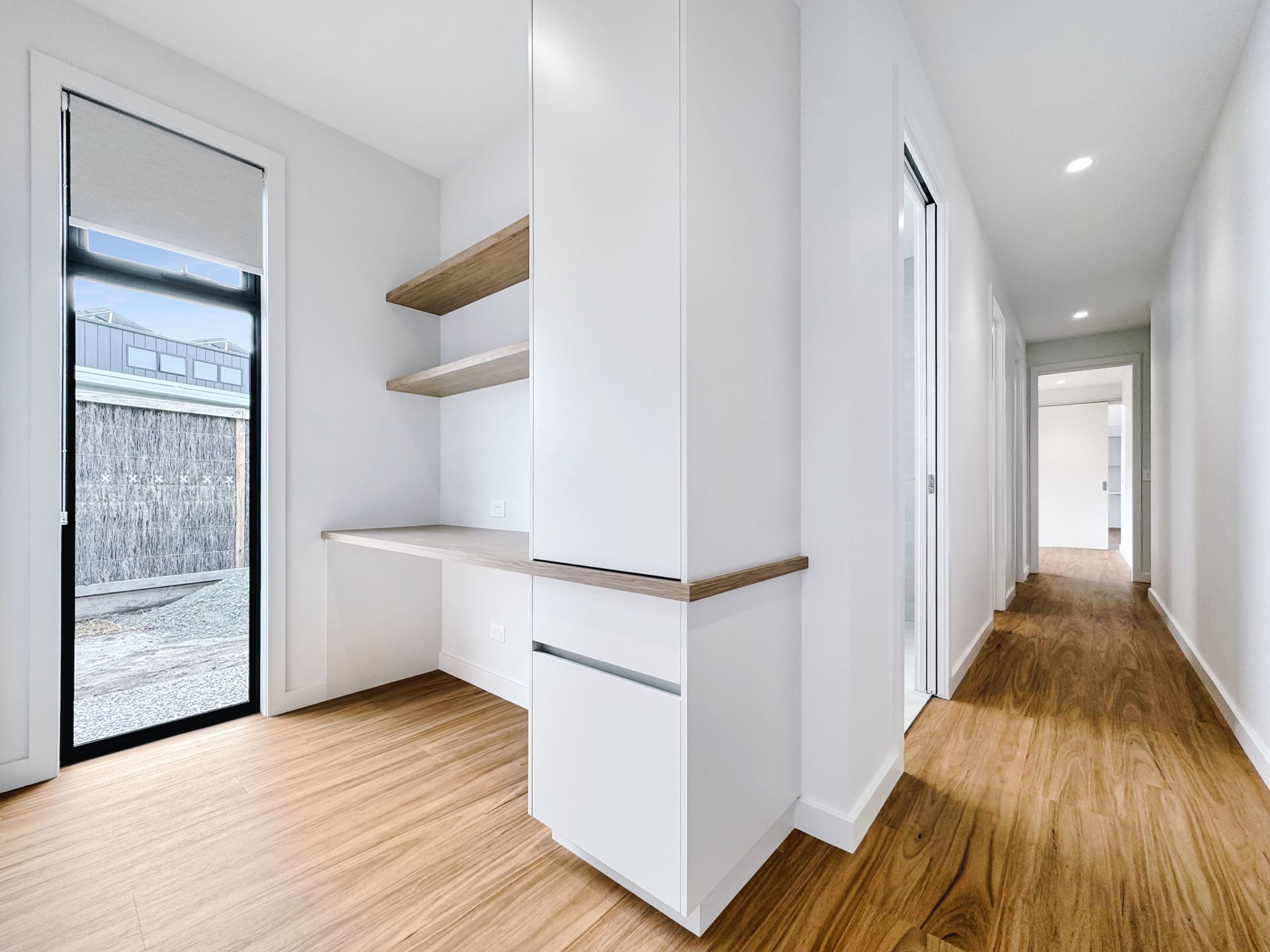 A hallway in a house with hardwood floors and a desk.