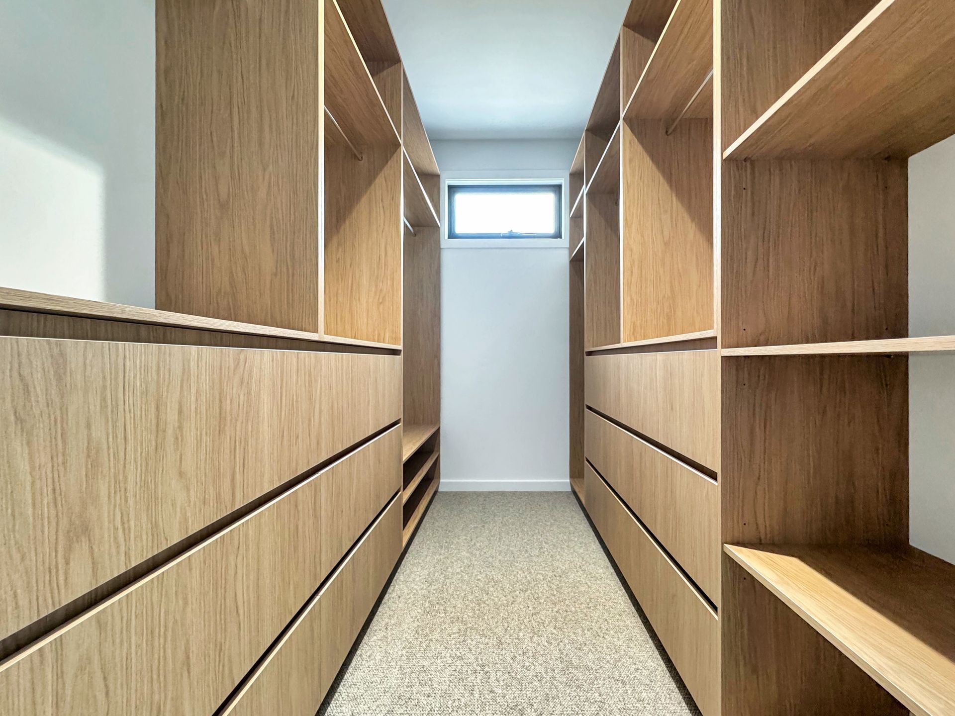 A walk in closet with lots of wooden shelves and drawers.