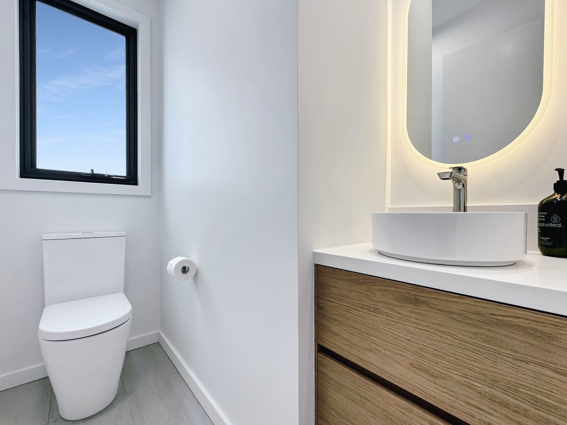 A bathroom with a toilet , sink , mirror and window.
