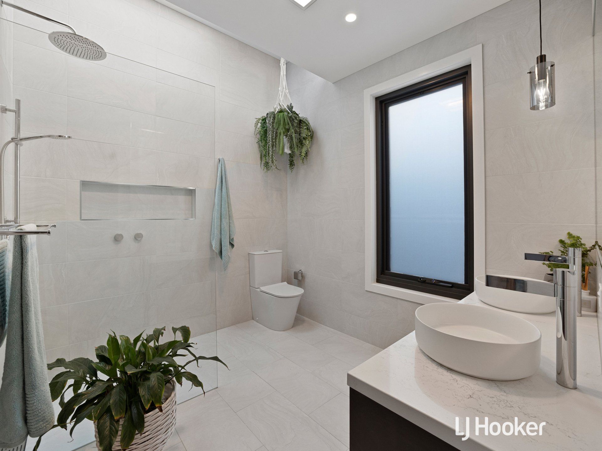 A bathroom with a sink , toilet , shower and window.