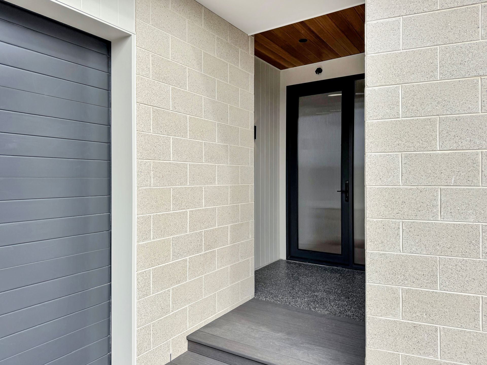 A white brick wall with a black door and a gray garage door.