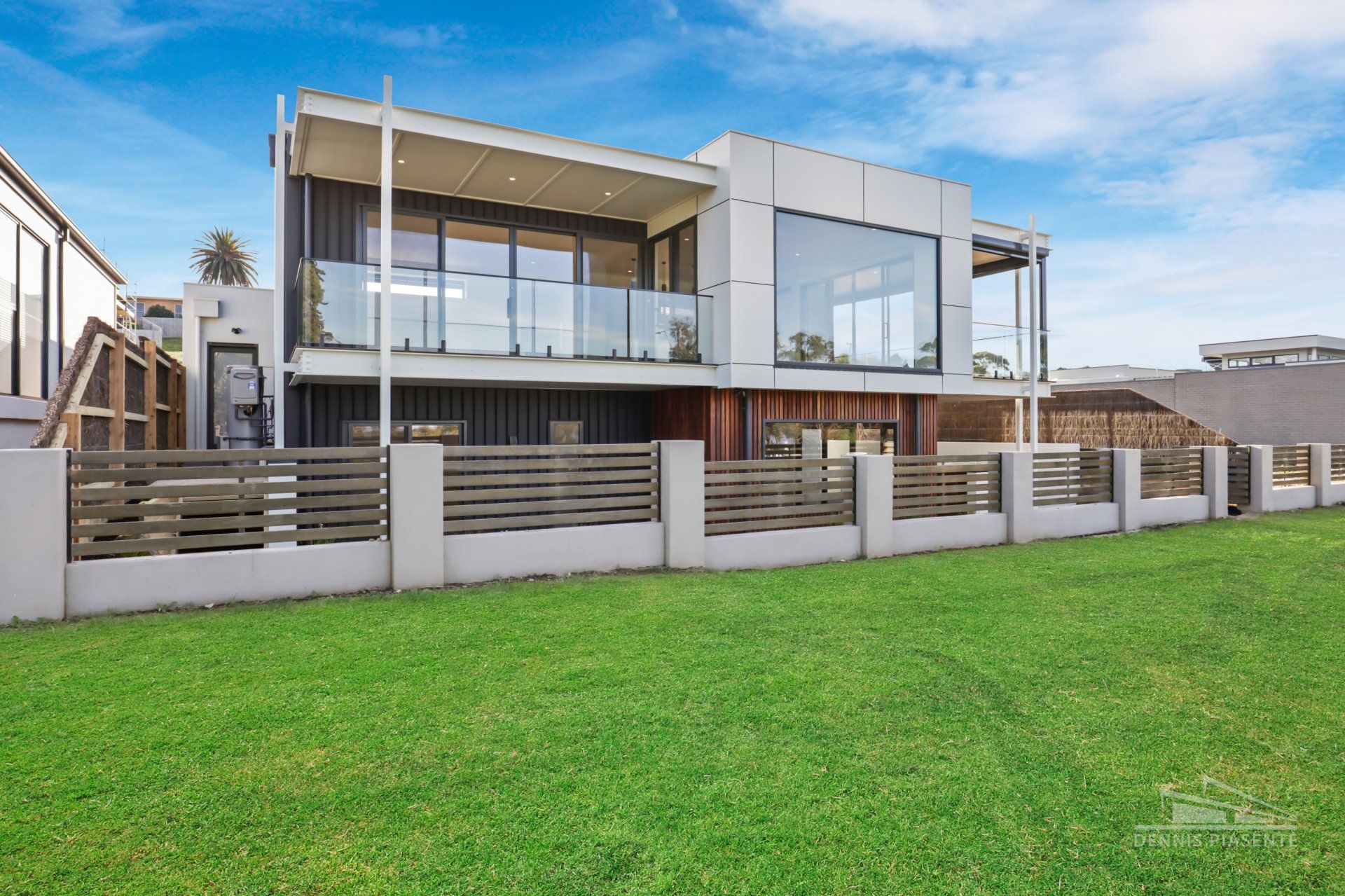 A large house with a fence and a lot of windows is sitting on top of a lush green field.