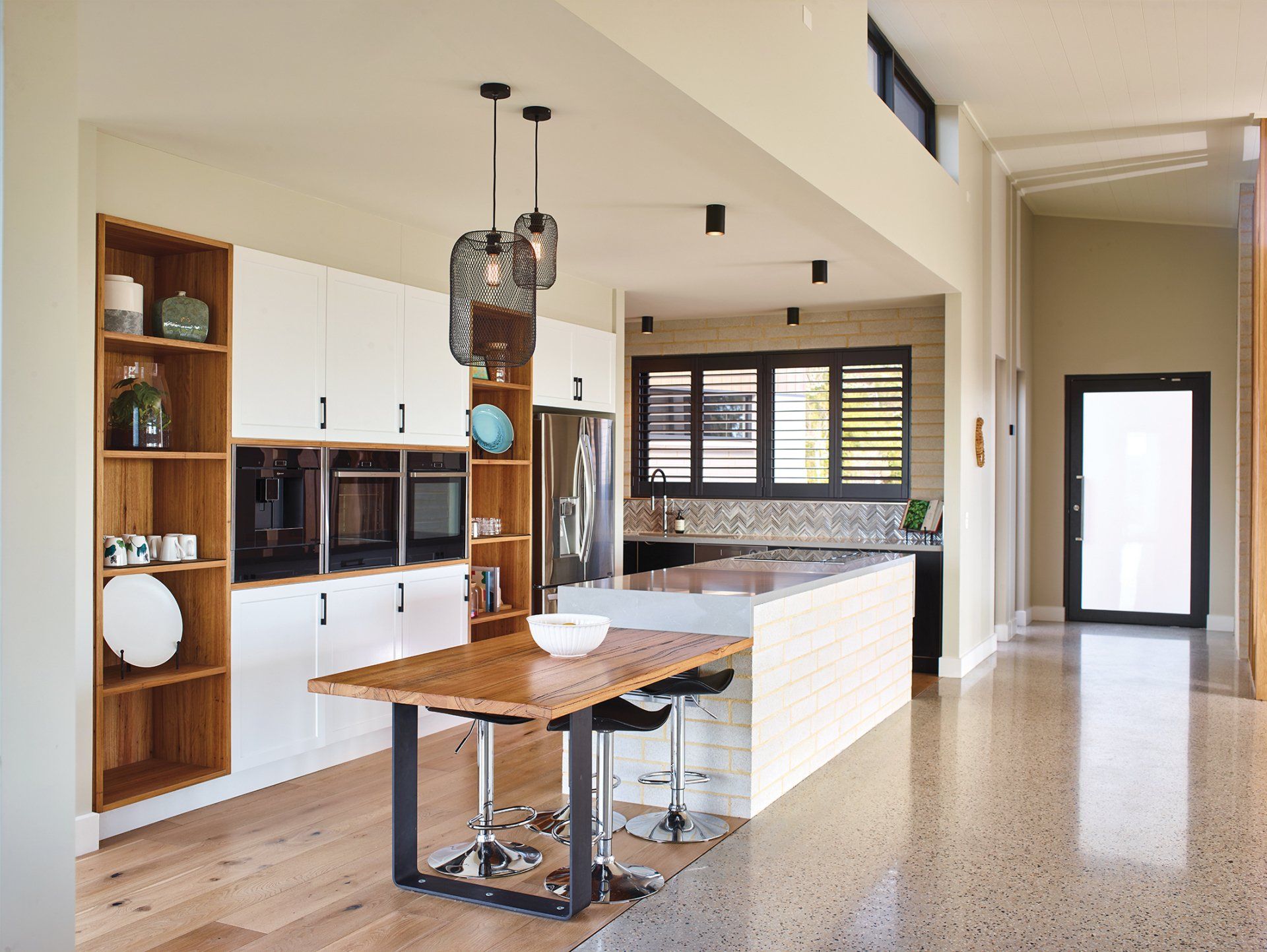 A kitchen with white cabinets , a wooden table and stools.
