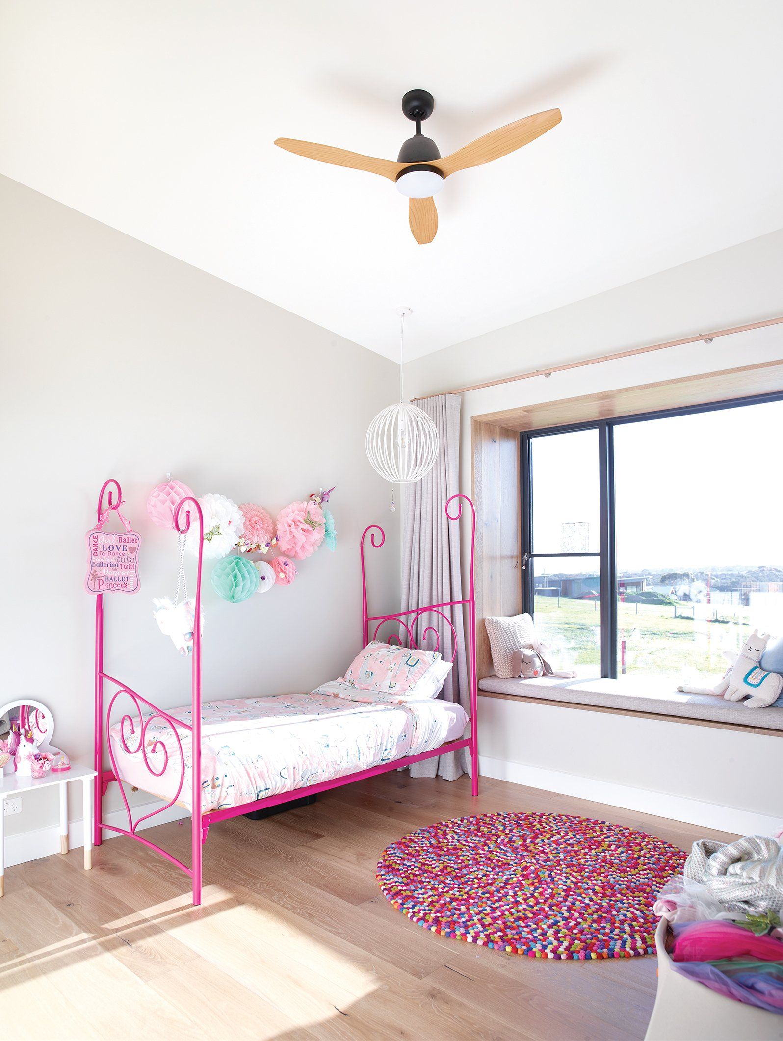 A girl 's bedroom with a pink bed and a ceiling fan.