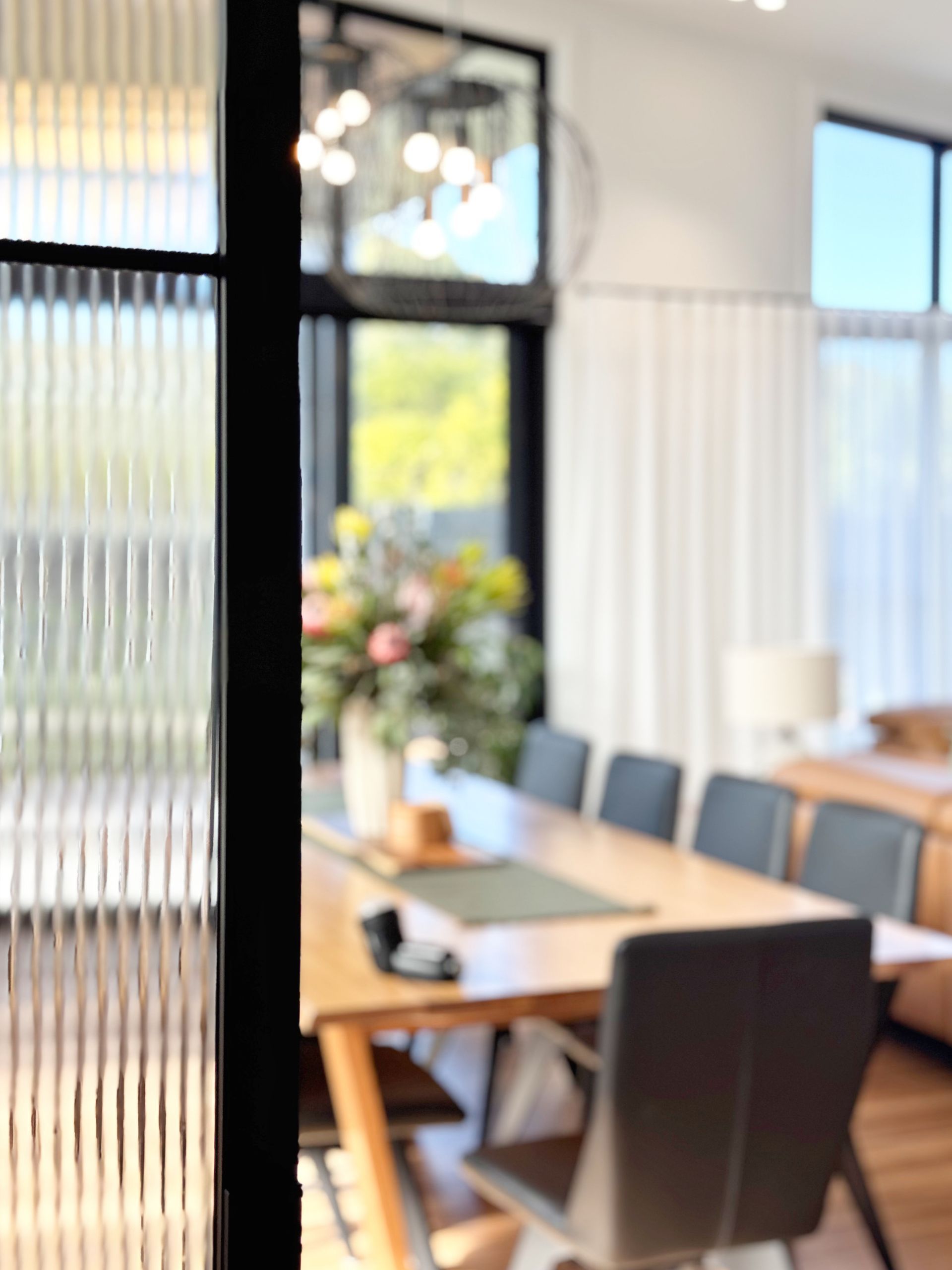 Dining room interior with a long wooden table, chairs, and a textured glass door.
