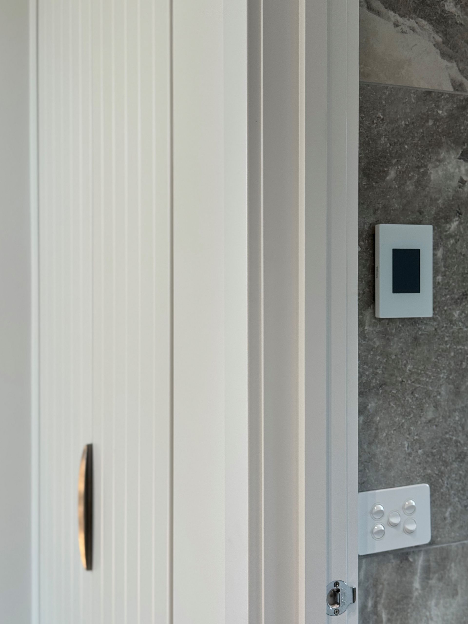 White cabinet door with dark handle next to a wall with a thermostat and light switch.