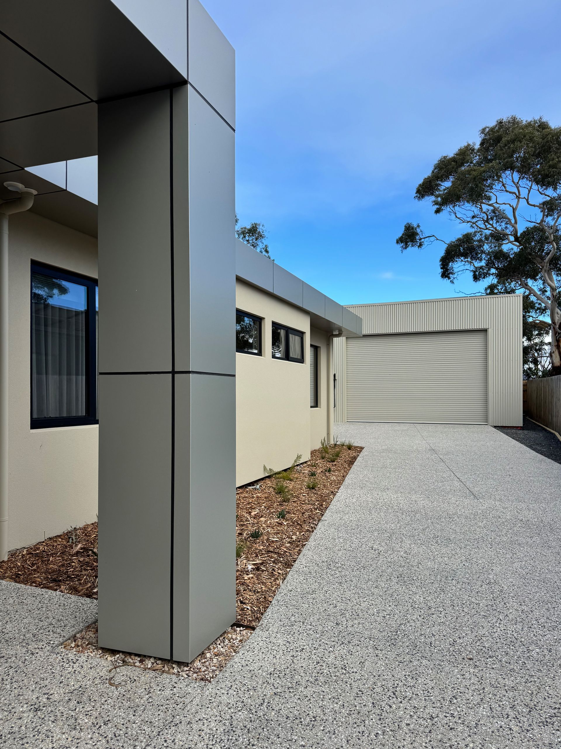 Modern house exterior with gray gravel driveway, beige walls, and a blue sky.