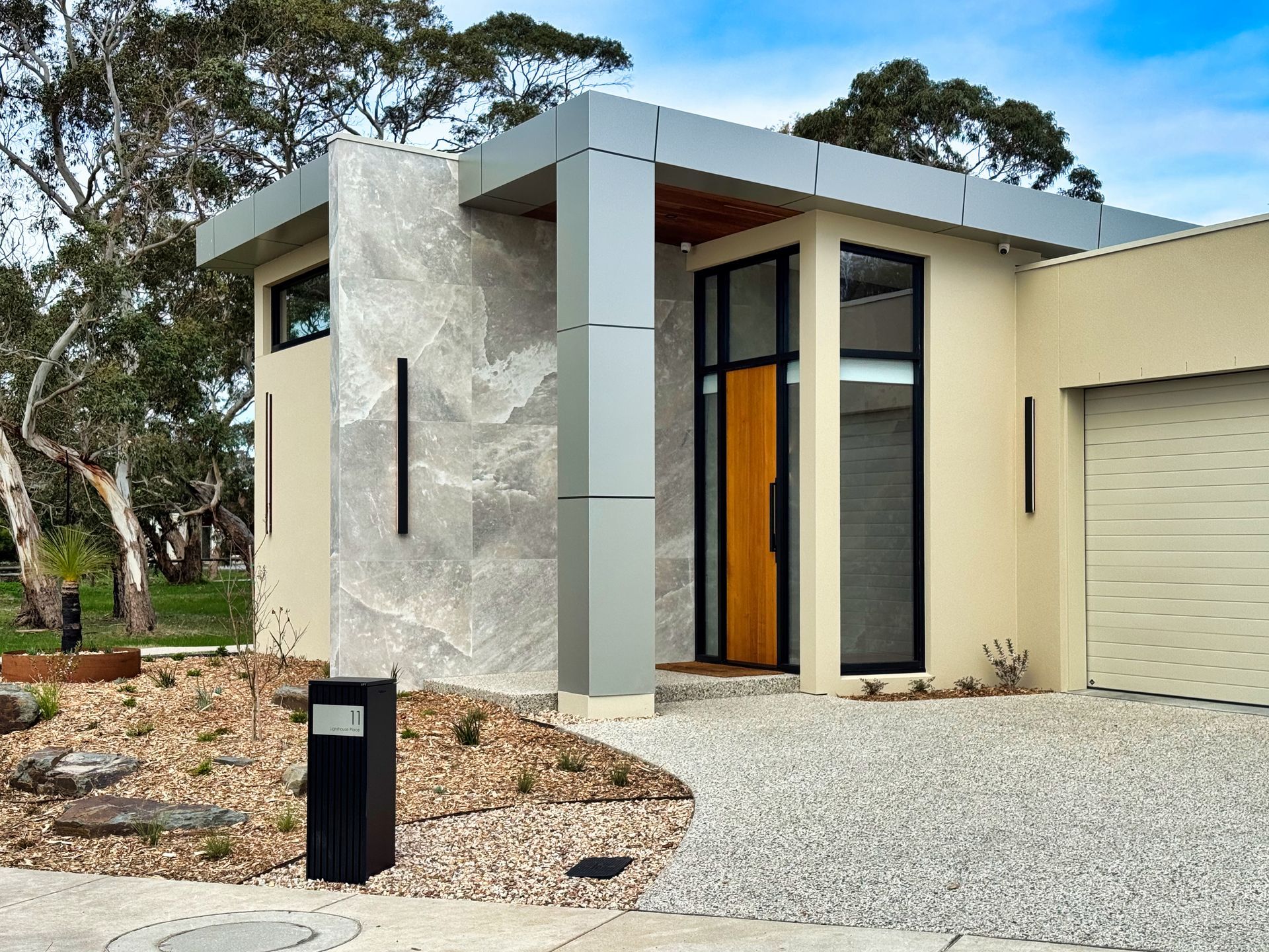Modern home with gravel driveway, stone facade, and black accents.