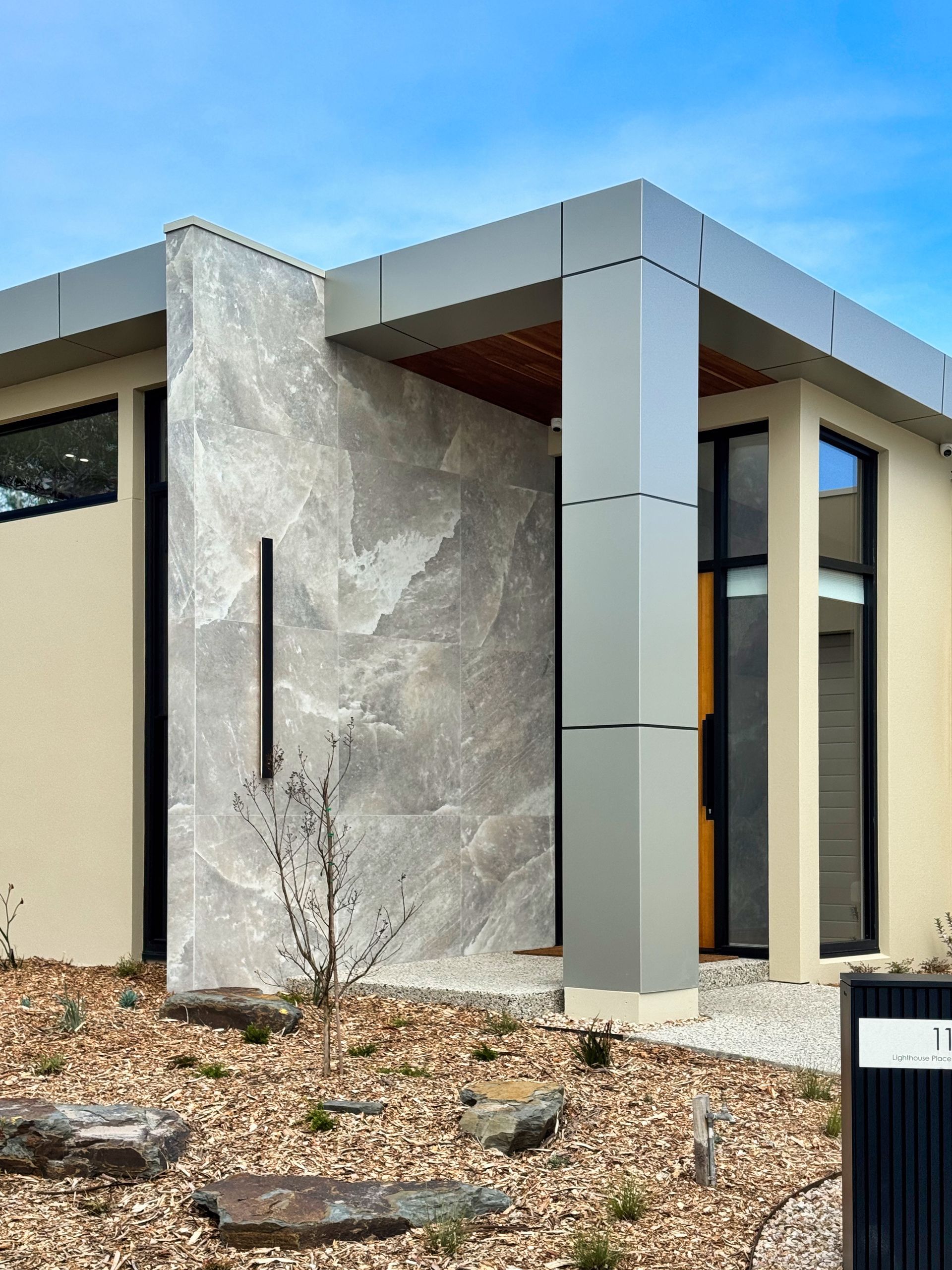 Modern home exterior with stone wall and grey accents, under blue sky.