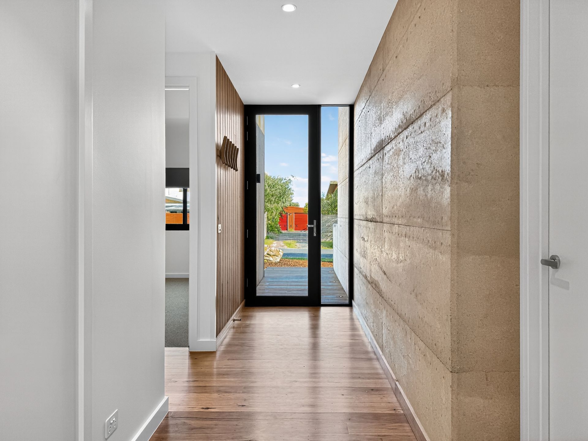 Hallway with wooden floor, textured wall, and glass door leading to a backyard.