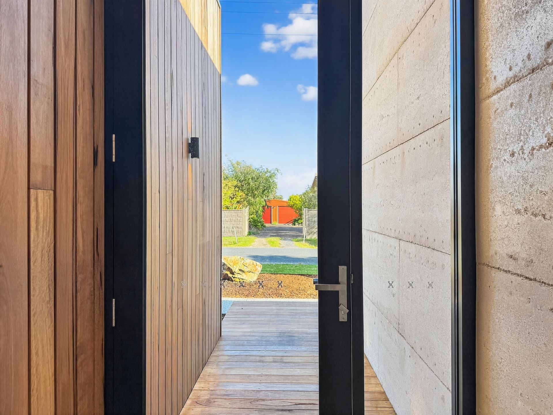 Wooden entryway with open door revealing a street and blue sky.