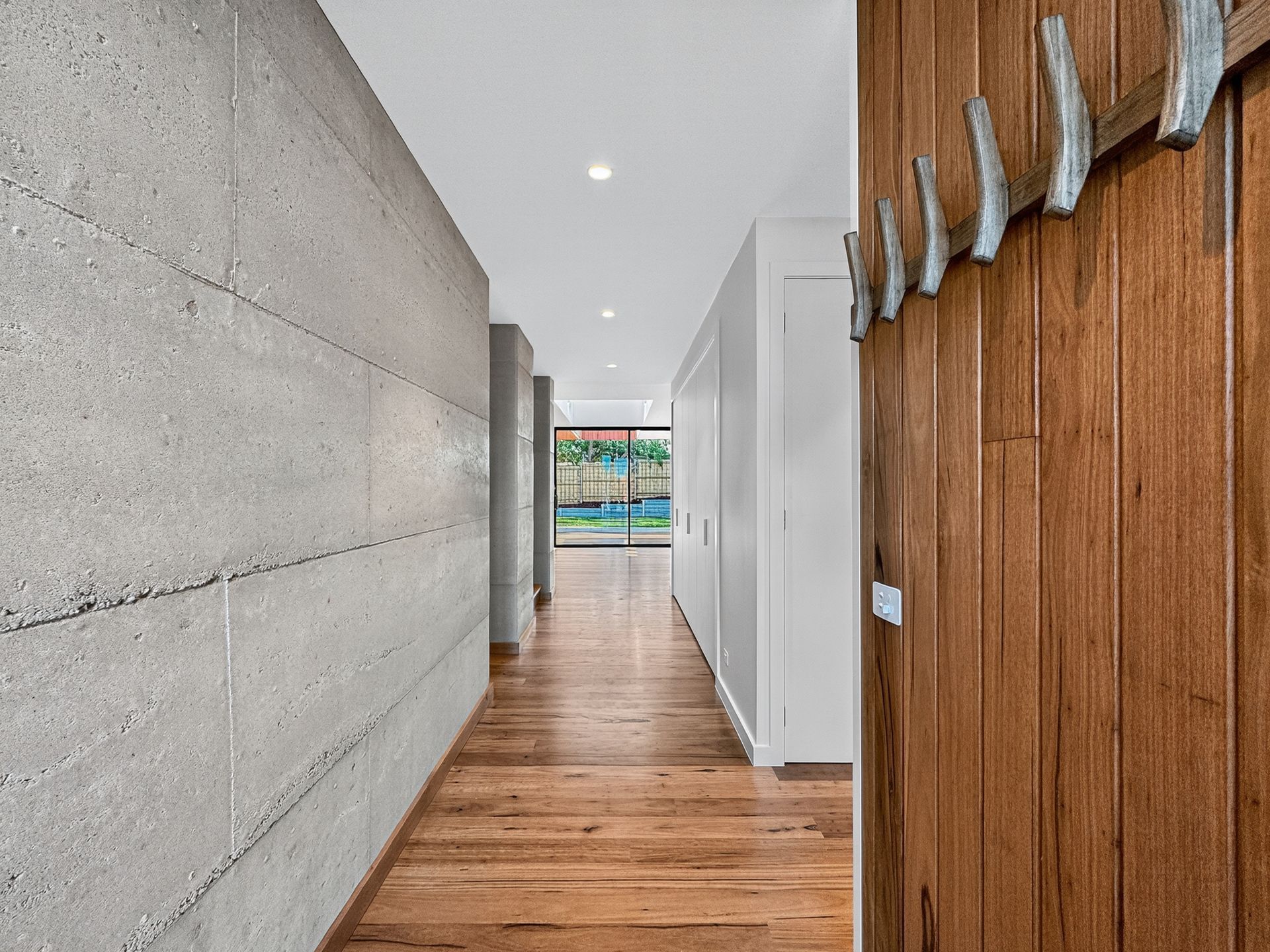 Hallway with a concrete wall on the left, wooden floor, and a wooden door with hooks on the right.