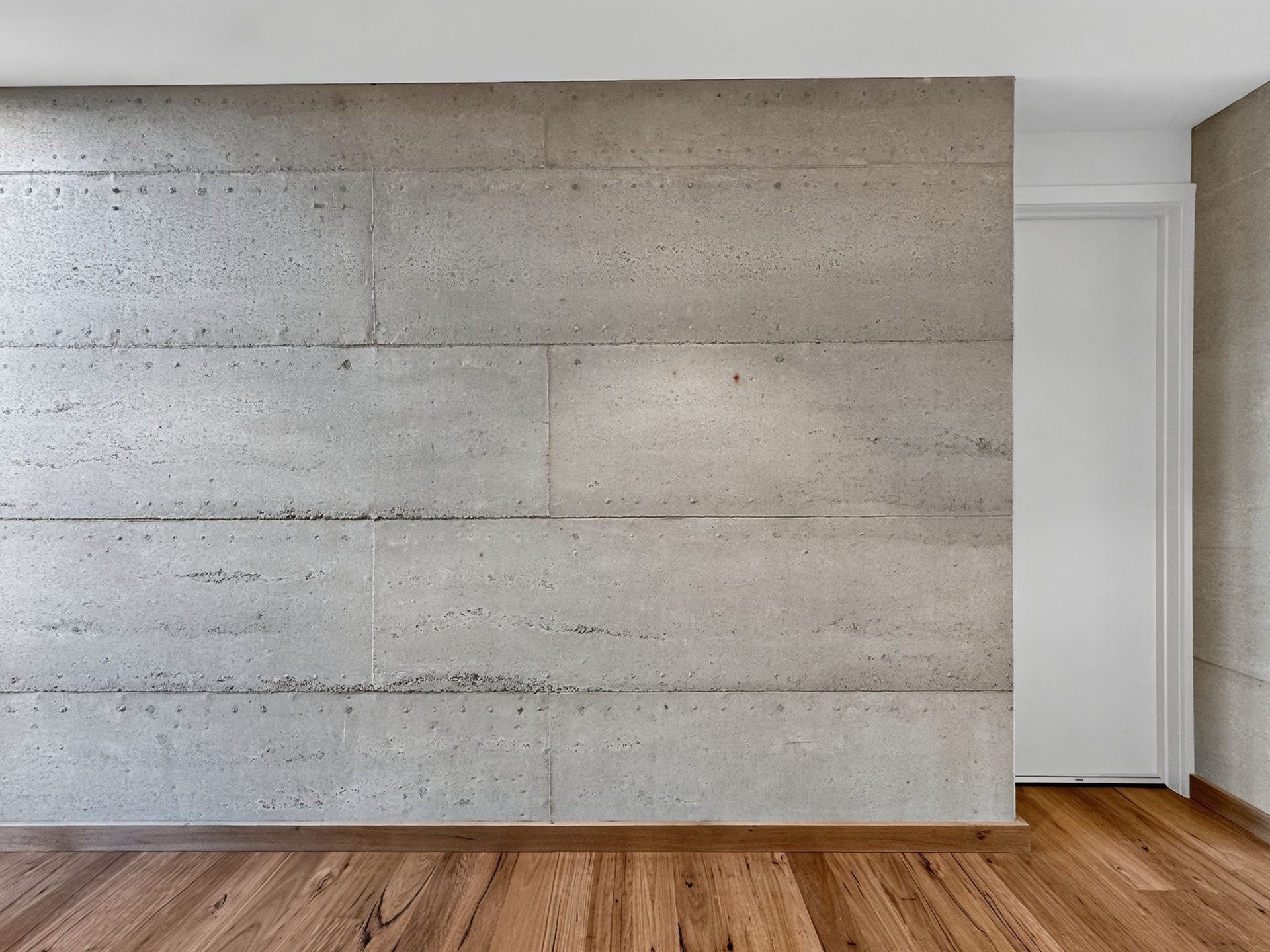 Concrete wall with horizontal lines, a white door, and a wood floor.
