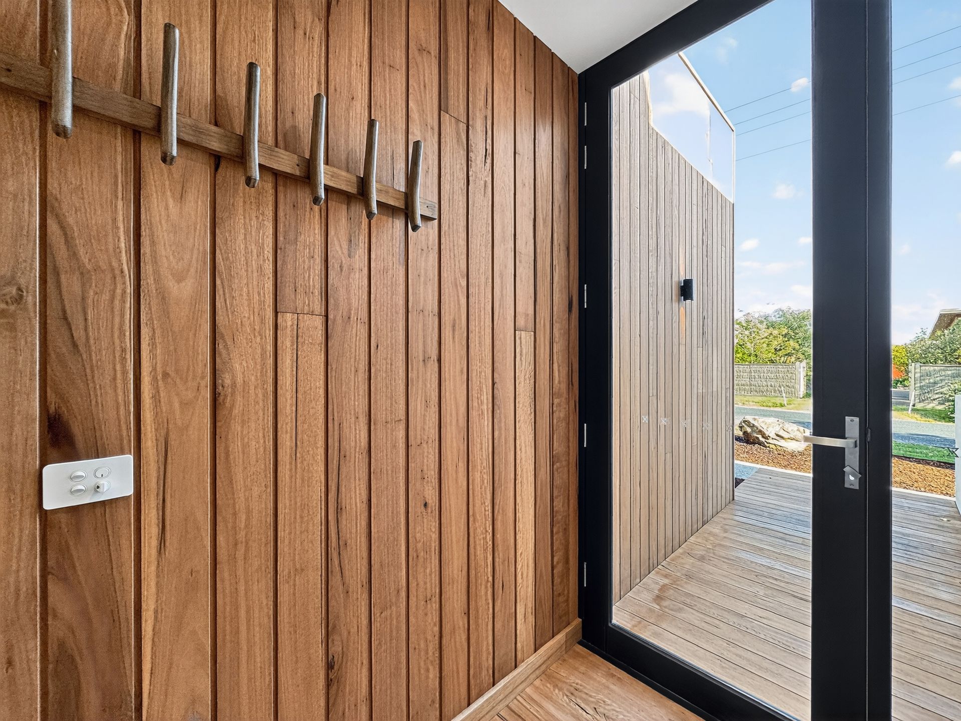 Wooden-walled entryway with coat rack and door to outdoor deck and fence.